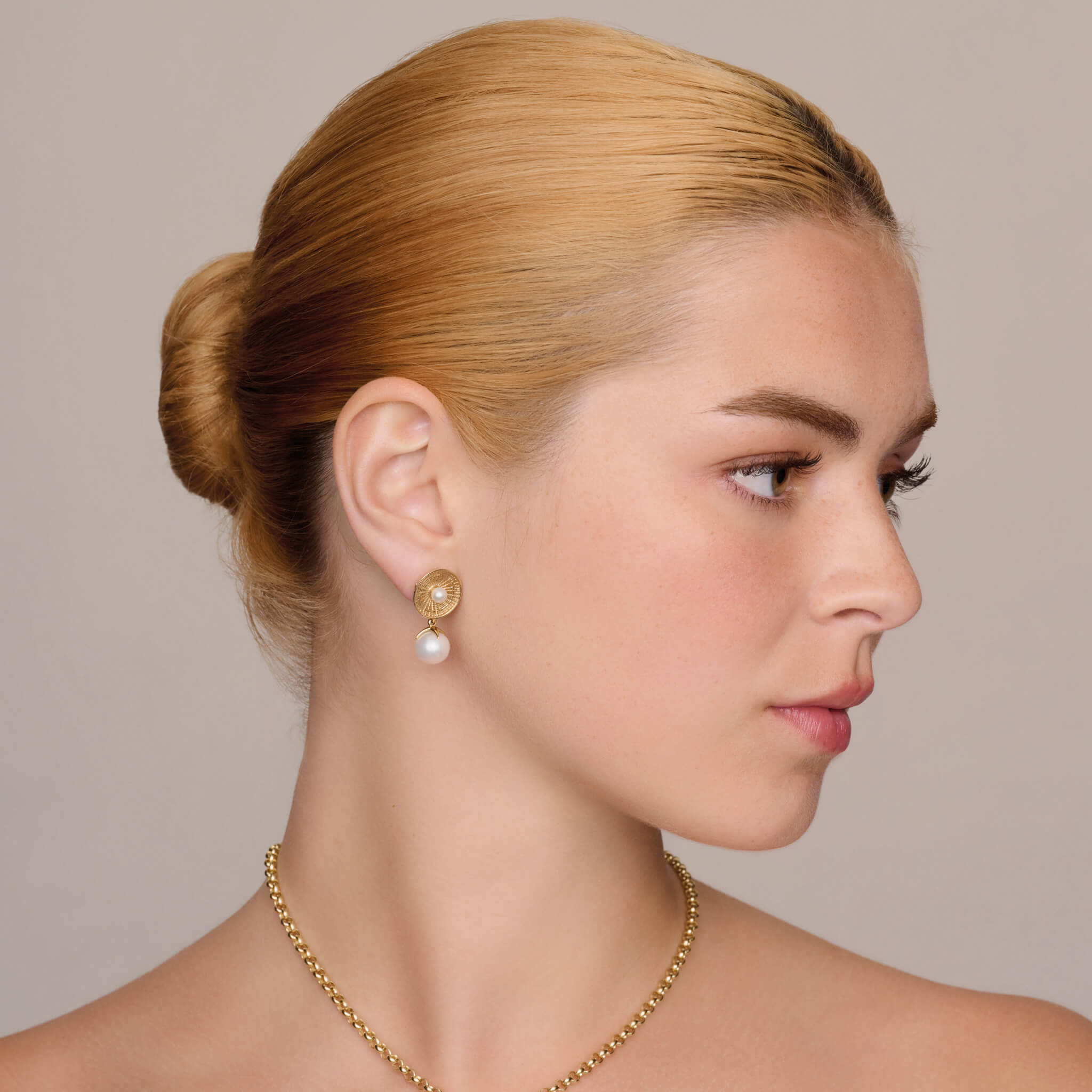model wears handcrafted Epidavros amphitheatre shaped earrings in yellow gold with a pearl in the center, and interchangeable earring pendants in yellow gold with pearl