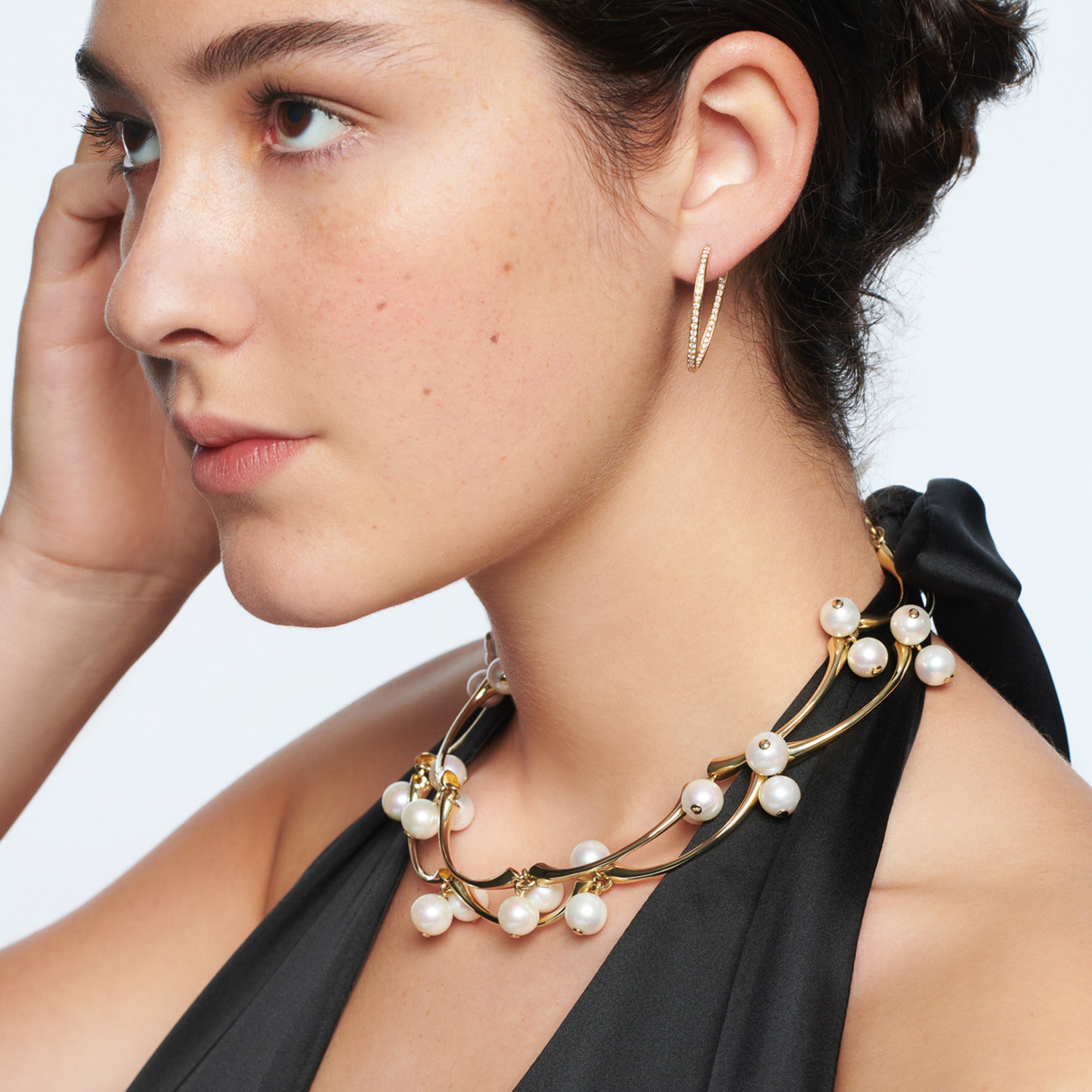 Model wearing a handcrafted yellow gold necklace in the shape of waves with pearls.