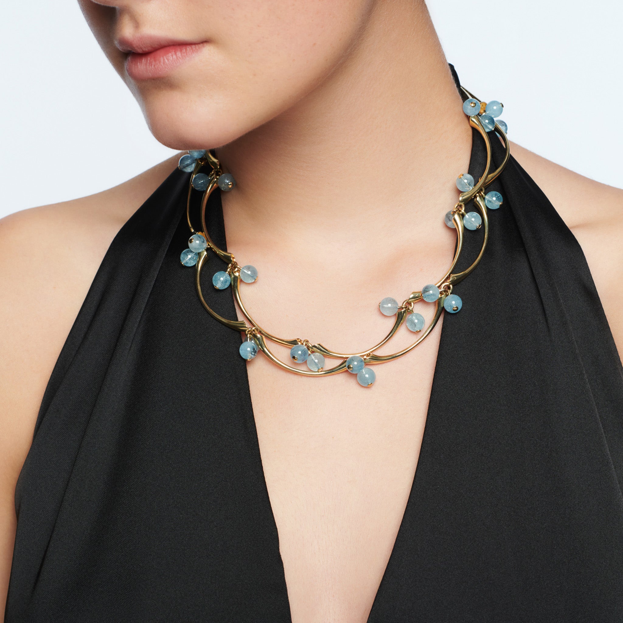 Model wearing a handcrafted yellow gold necklace in the shape of waves with aquamarines.