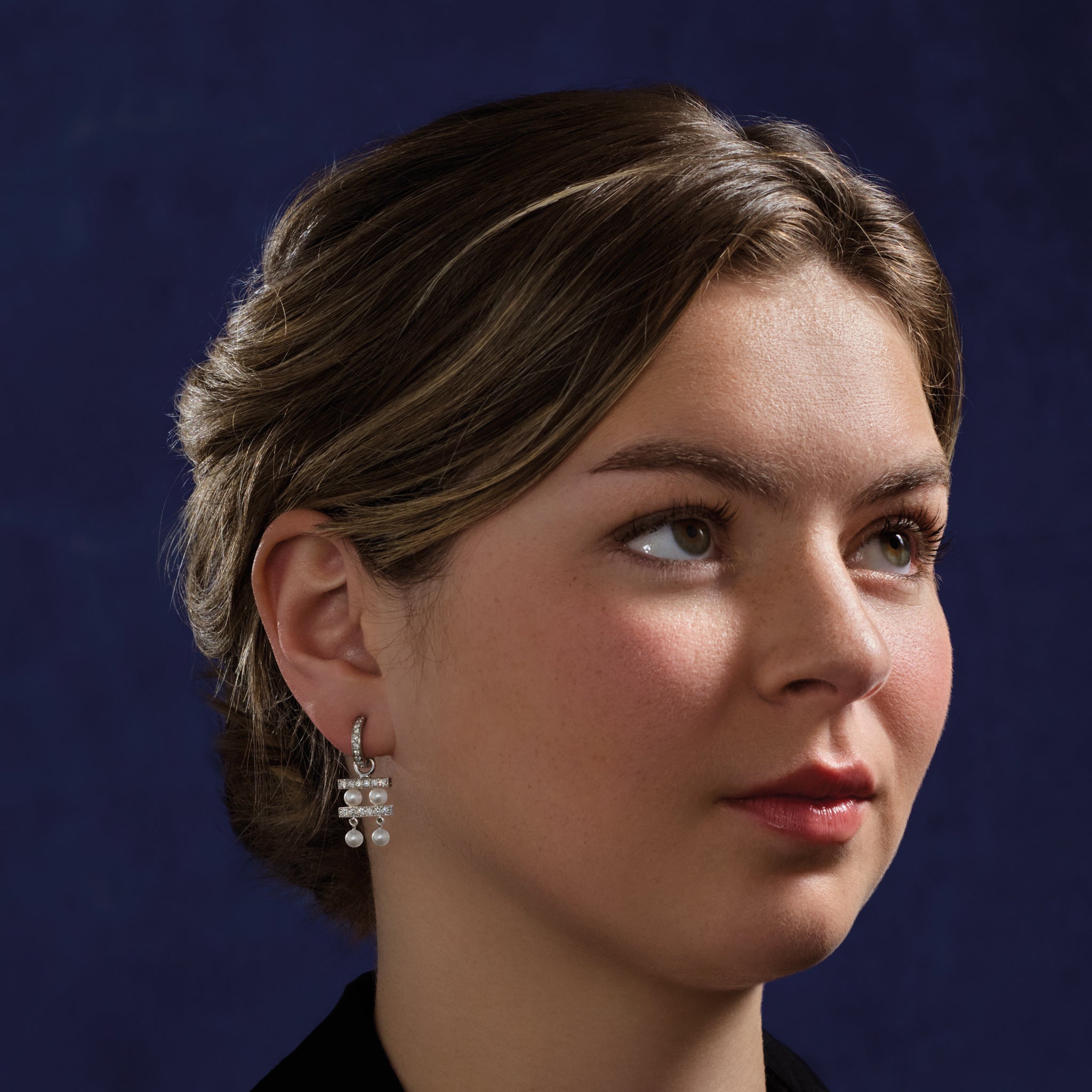 Model wearing handcrafted white gold earring drops with two tiers of pearls separated by delicate gold lines adorned with diamond pavé.