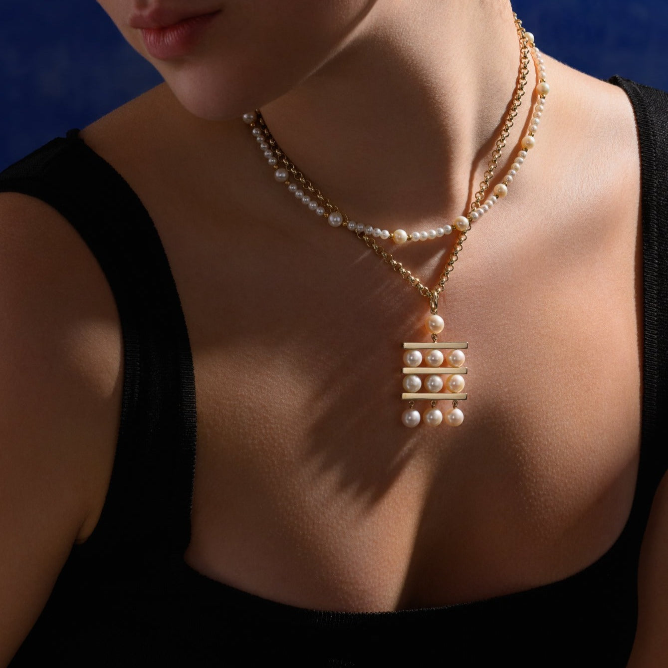 Model wearing a handcrafted yellow gold necklace pendant with three tiers of pearls separated by delicate yellow gold lines.