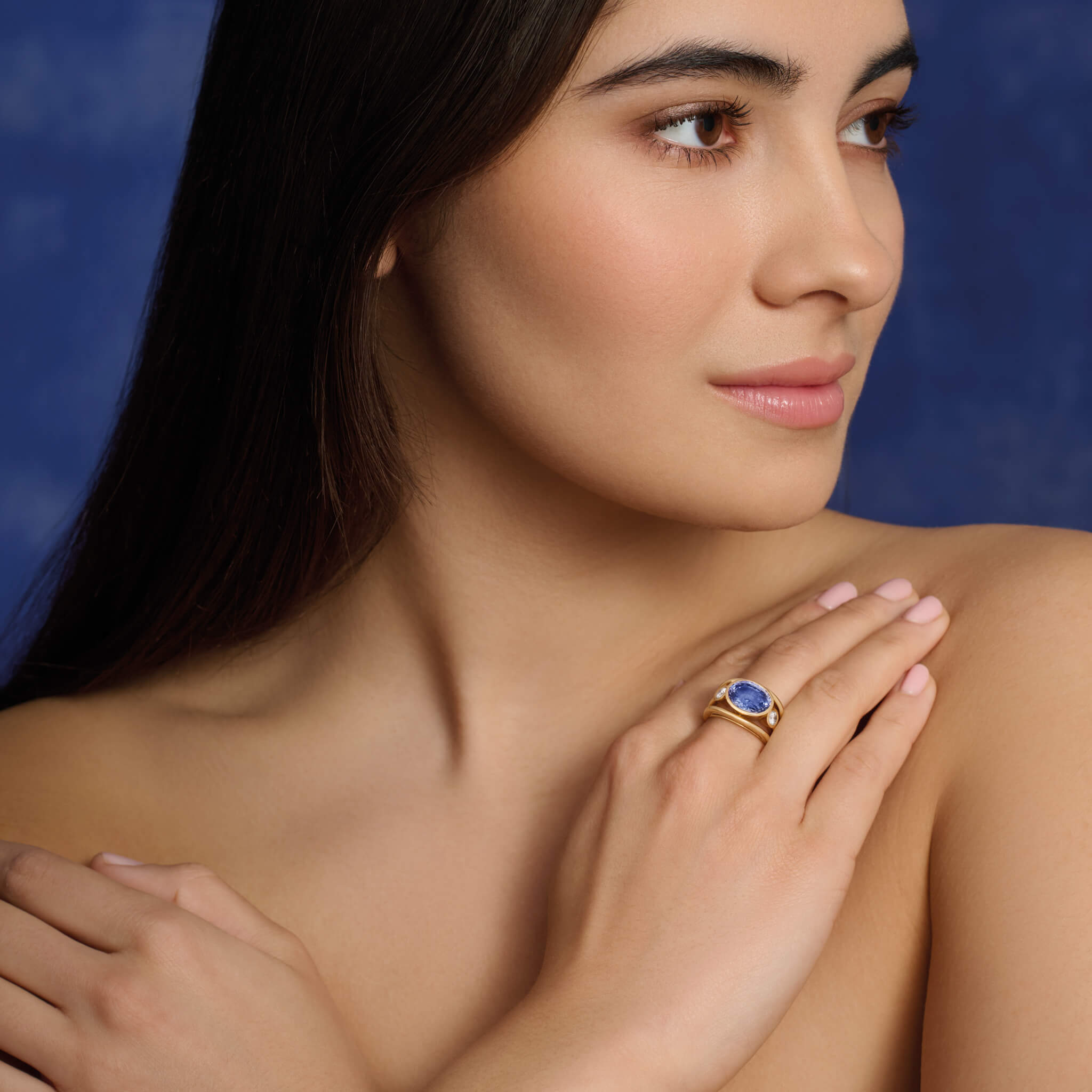 Model wearing handcrafted 18ct yellow gold ring with a central sapphire, the birthstone of September, flanked by two round diamonds.
