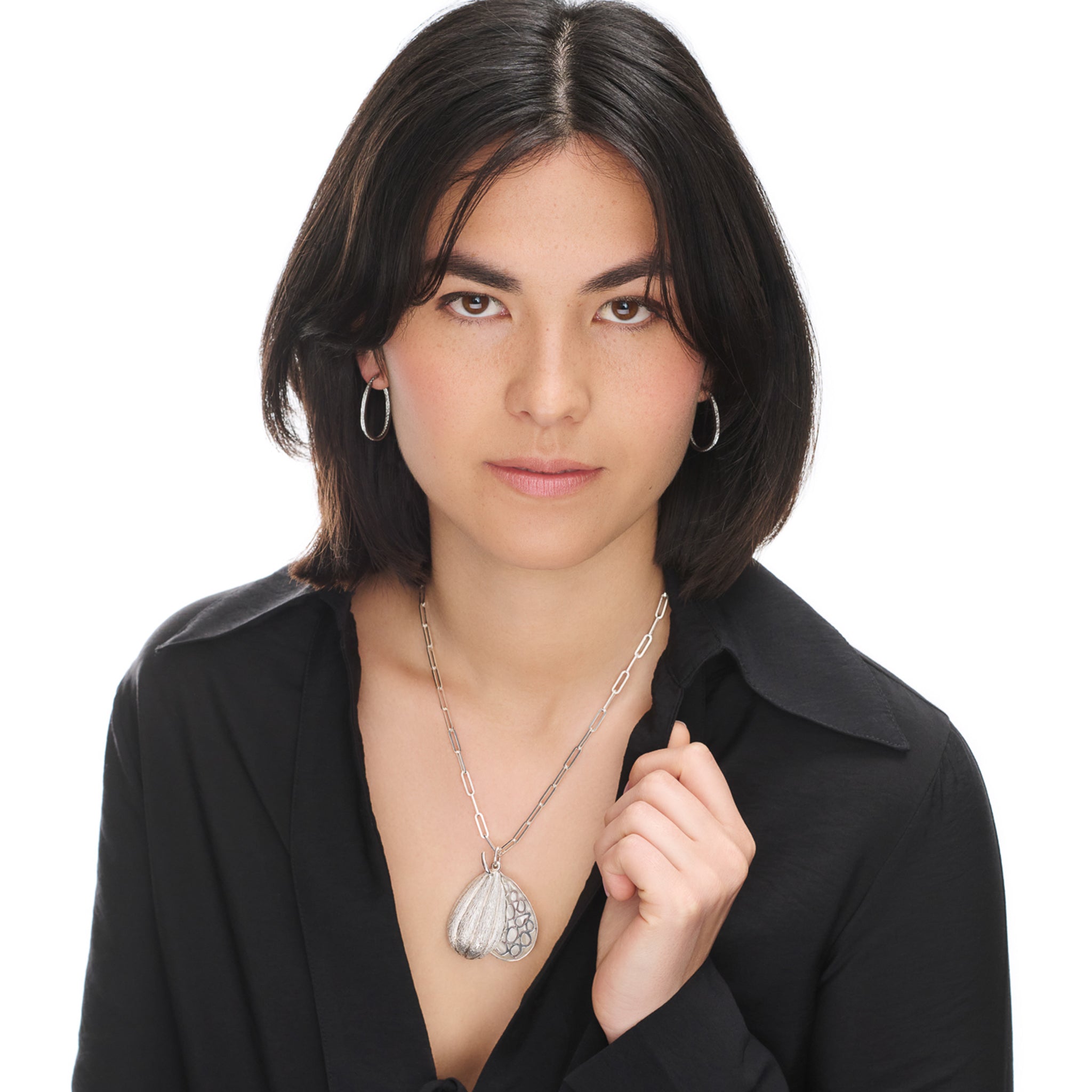 Model wearing handcrafted sterling silver necklace pendant in the shape of a cocoa pod which swivels open.