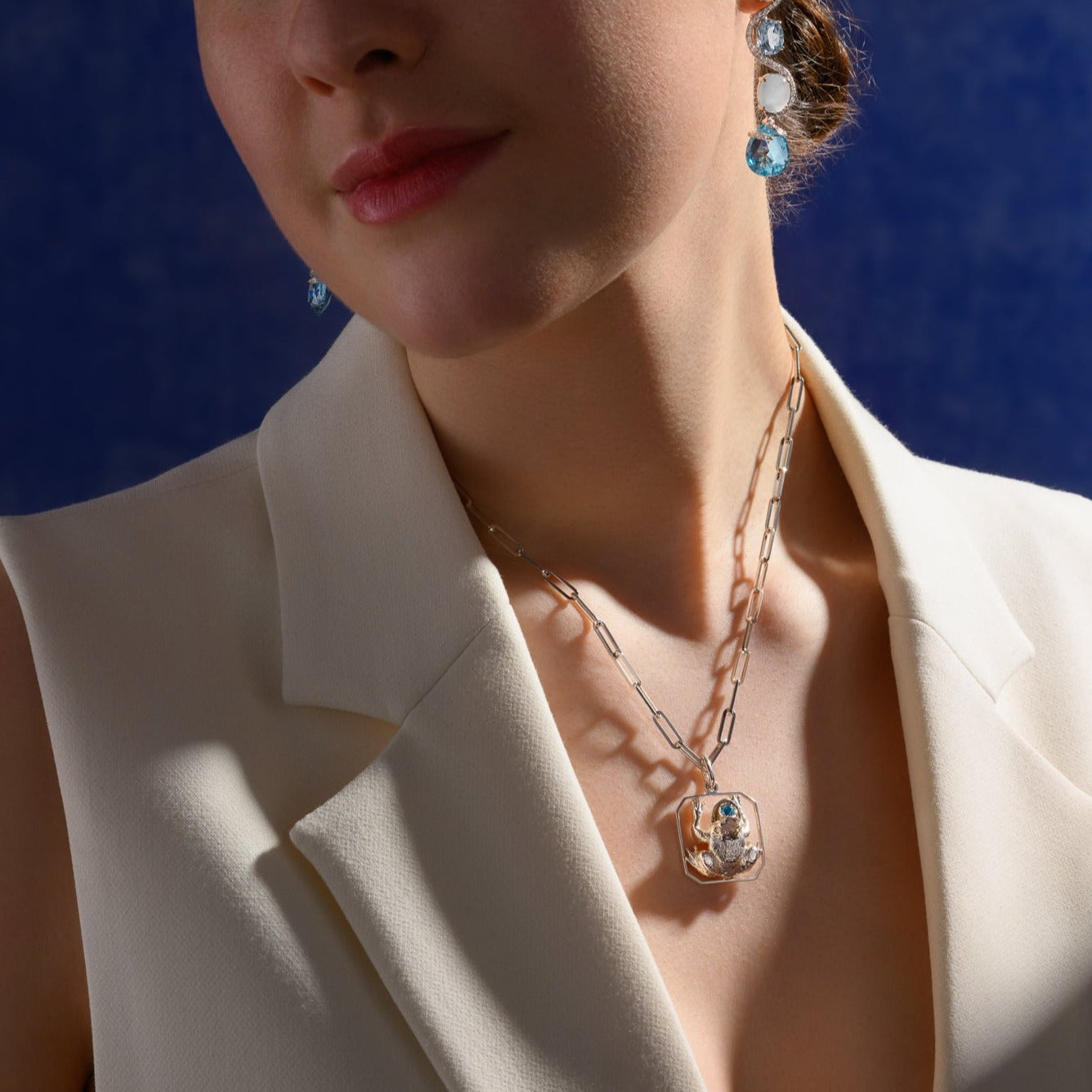 Model wearing a handcrafted sterling silver frog shaped necklace pendant with diamonds and blue topaz.
