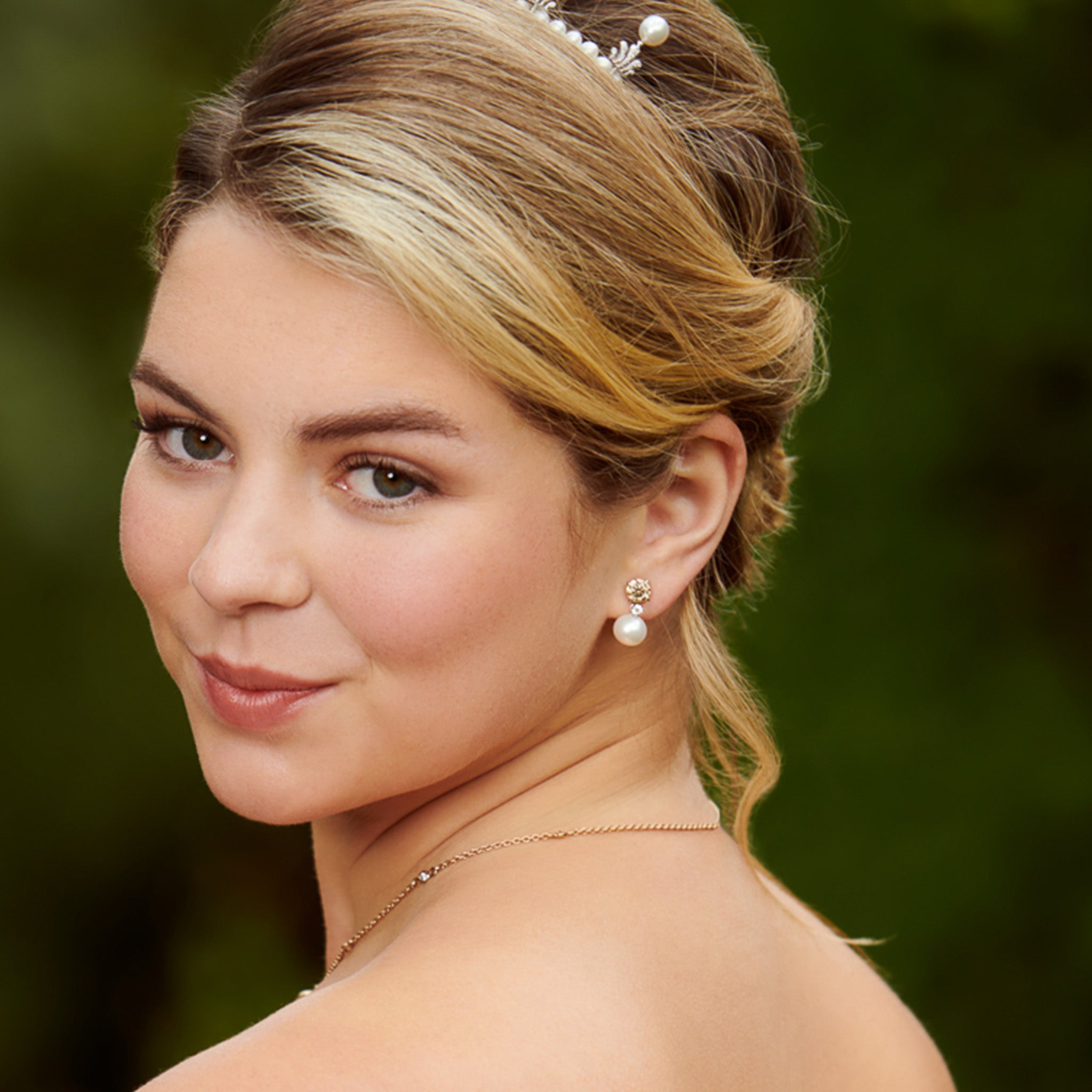 Model wearing handcrafted yellow gold halo earring drops with a pearl and diamond.