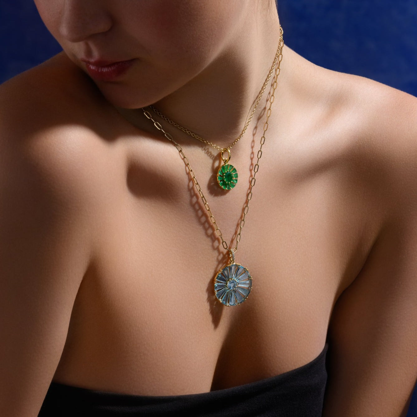 Model wearing a handcrafted yellow gold circular necklace pendant with baguette cut blue topaz and diamond gemstones.
