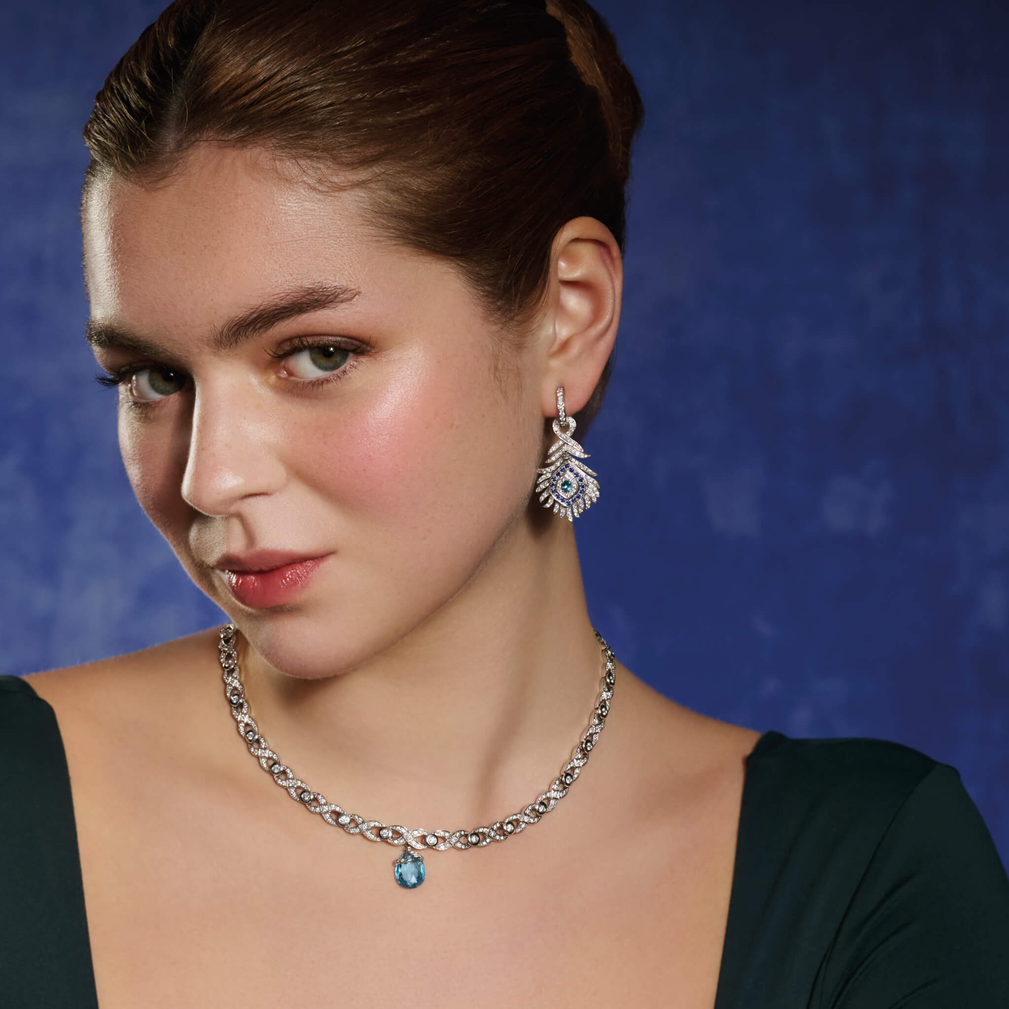 Model wears handcrafted 18ct white gold earring drops featuring a peacock feather shape with sapphires, aquamarines and diamonds.