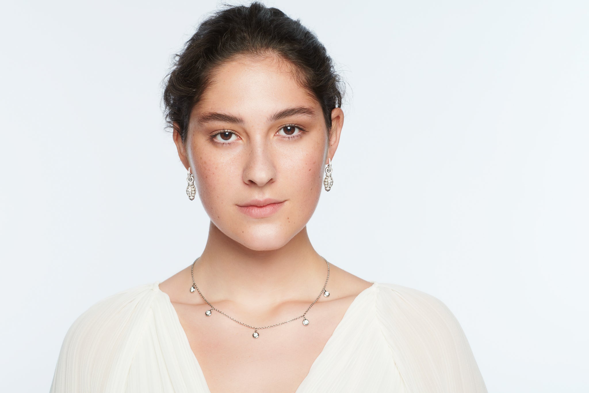 Model wearing a handcrafted white gold necklace featuring round precious gemstones, the Talya design.
