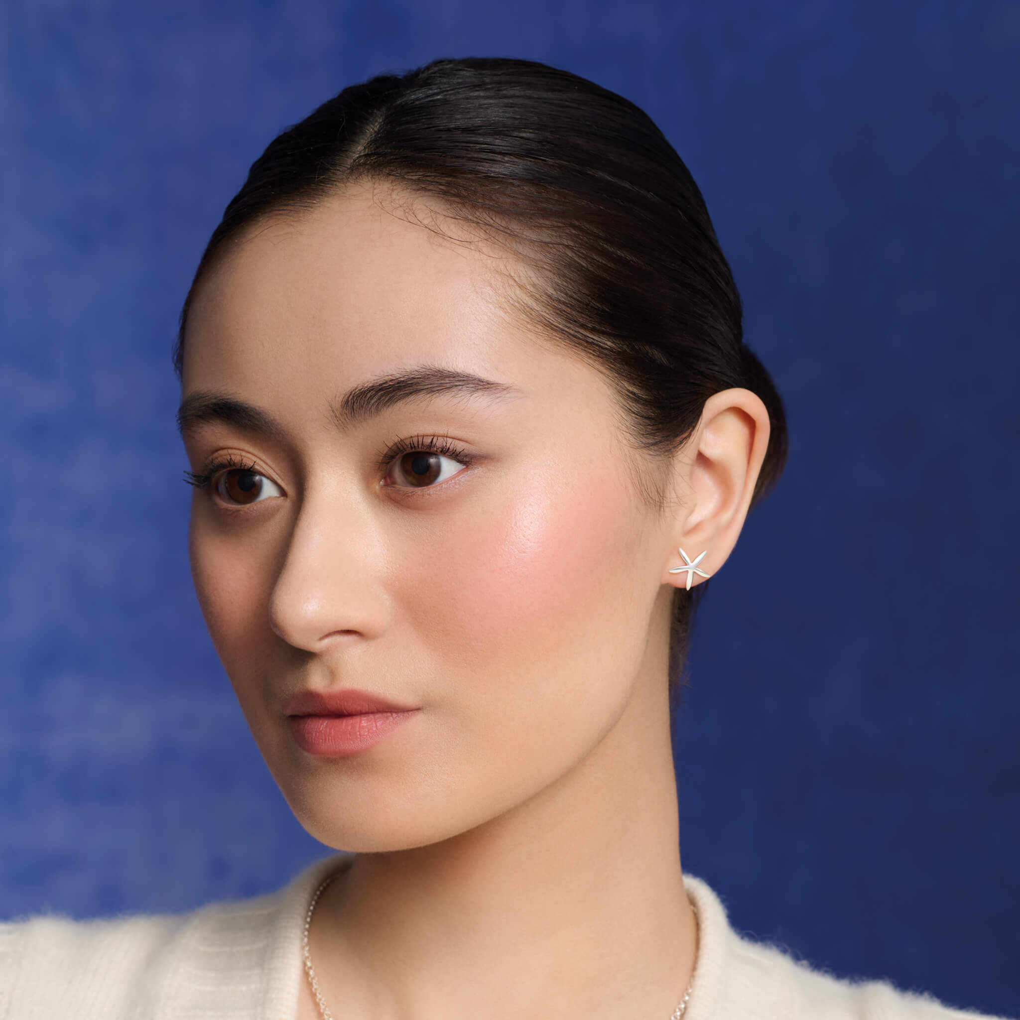 Model wearing handcrafted starfish shaped earrings in precious metal.