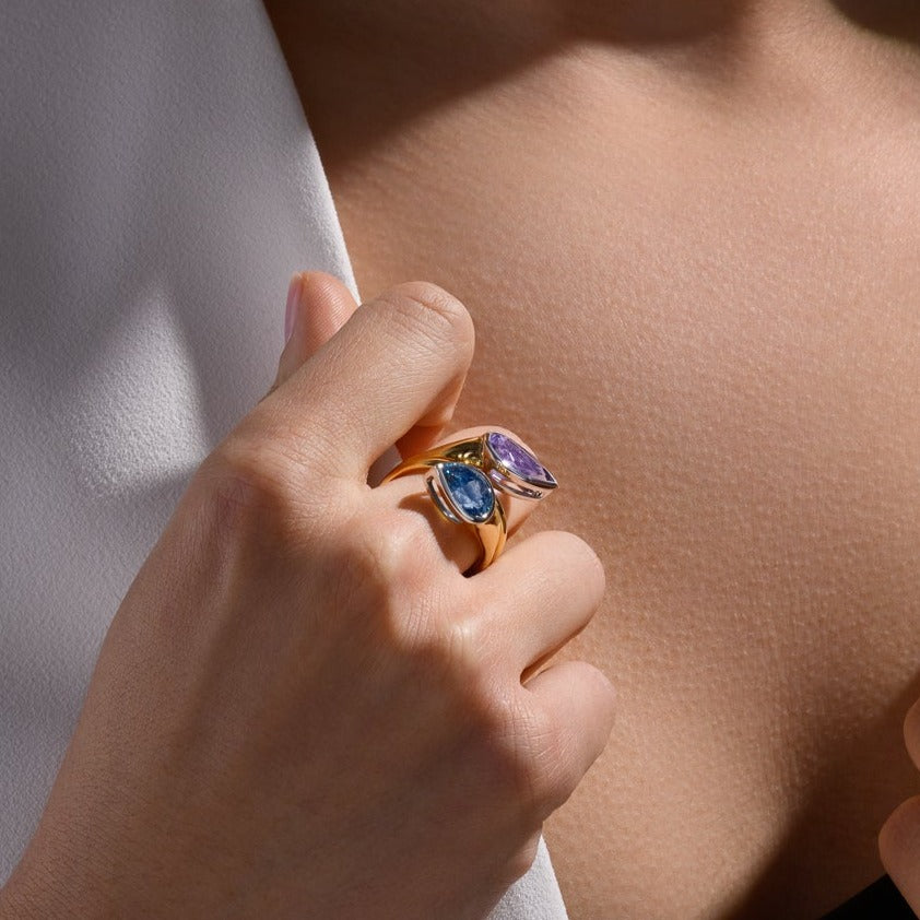 Model wearing a handcrafted 18ct yellow and white gold swirl ring featuring teardrop shaped purple tourmaline and aquamarine at each end.