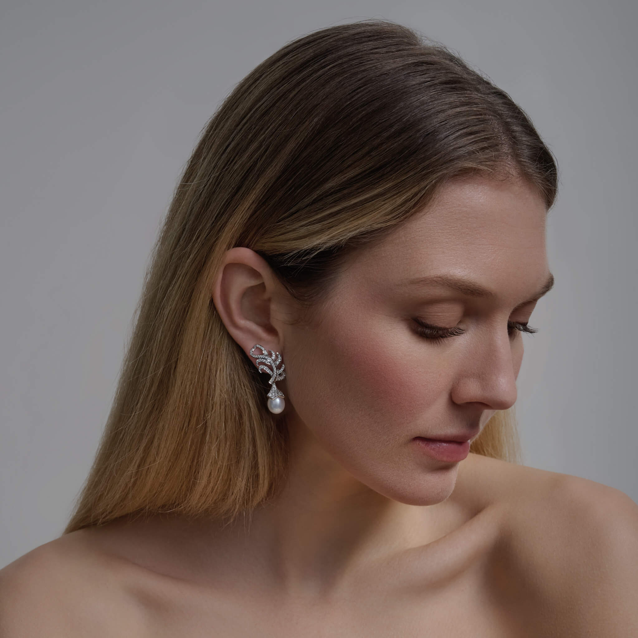 Model wears handcrafted earrings in the shape of a feather plume in 18ct white gold with diamond pavé and a detachable pearl drop.