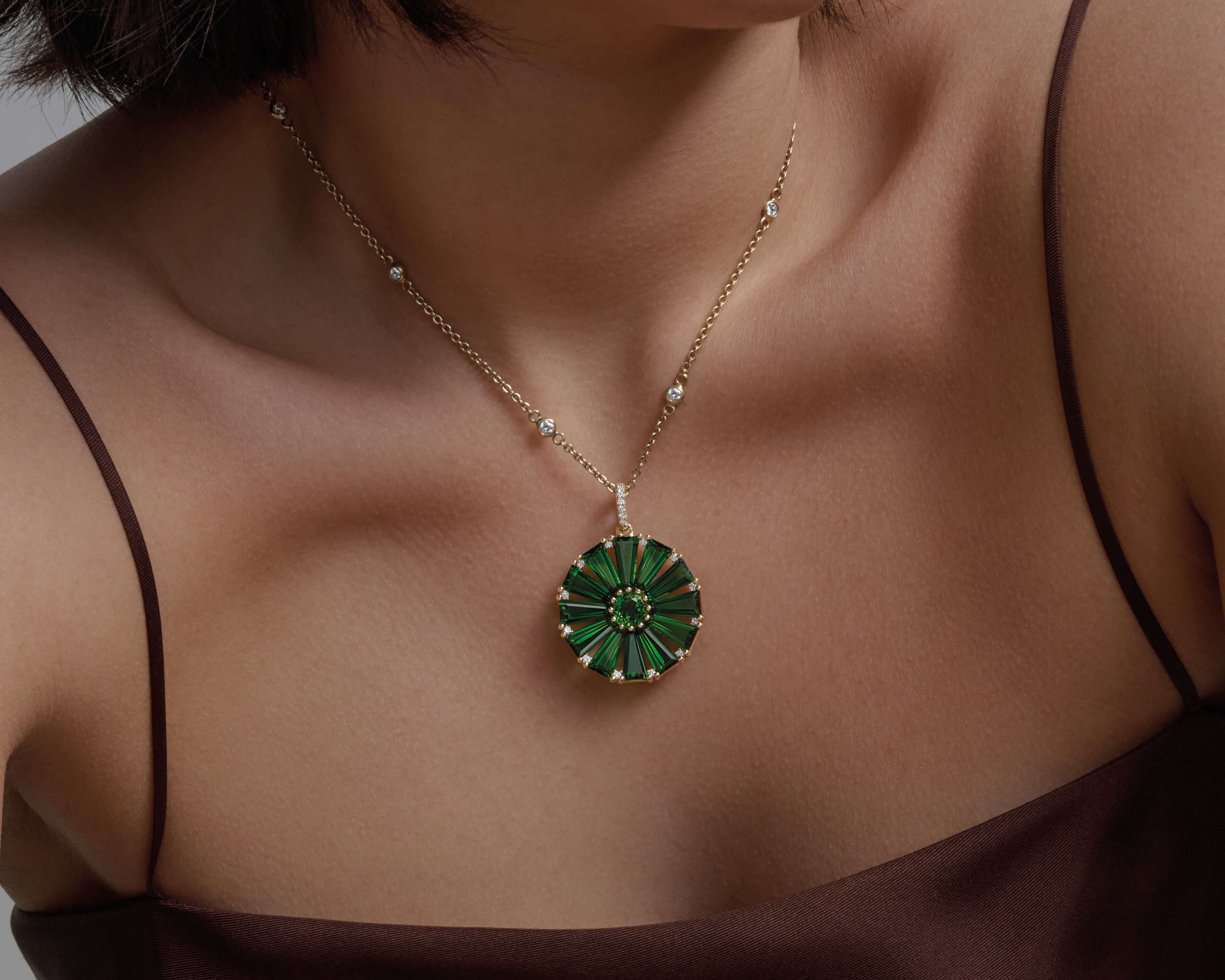 Model wearing a handcrafted yellow gold circular necklace pendant with baguette cut chrome diopside and diamond gemstones.