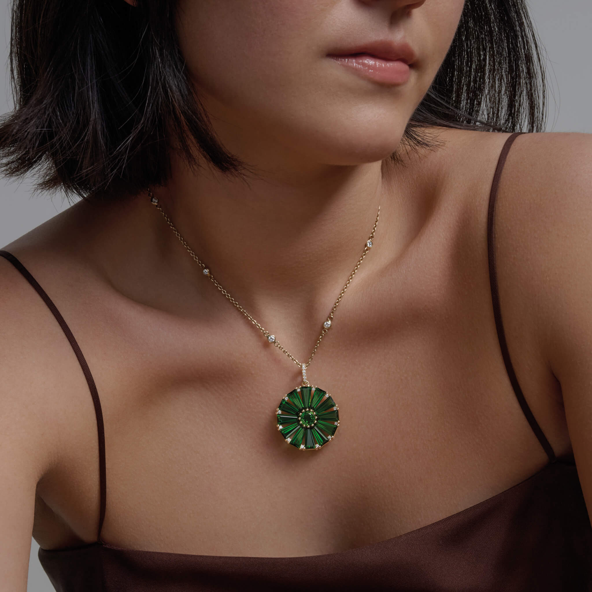 Model wearing a handcrafted yellow gold circular necklace pendant with baguette cut chrome diopside and diamond gemstones.