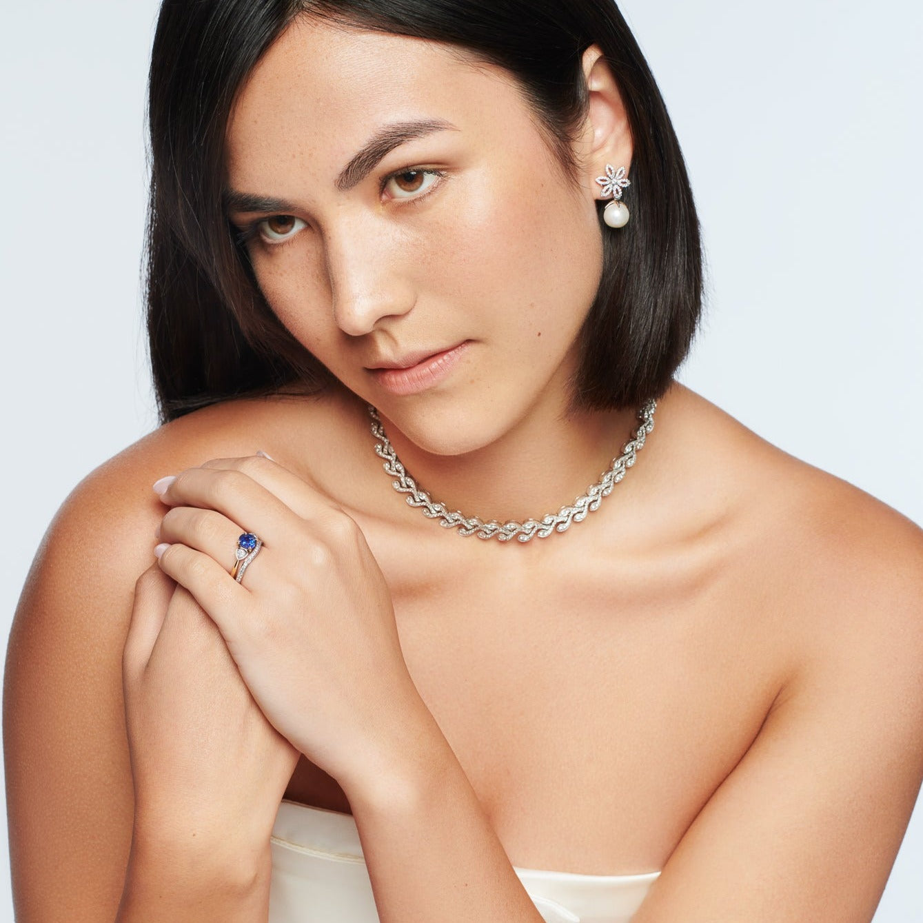 Model wearing handcrafted 18ct white and yellow gold engagement ring featuring a large central round sapphire flanked by one smaller teardrop-shaped diamond on each side.