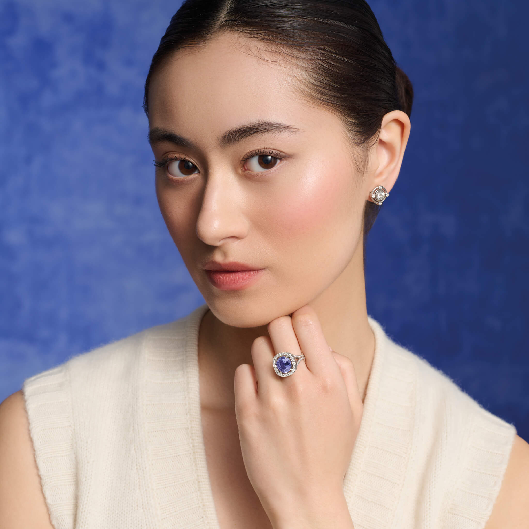 Model wears handcrafted 18ct white gold engagement ring featuring a large, cushion-cut dark blue tanzanite surrounded by a halo of small diamonds and smaller diamonds embedded along the band.