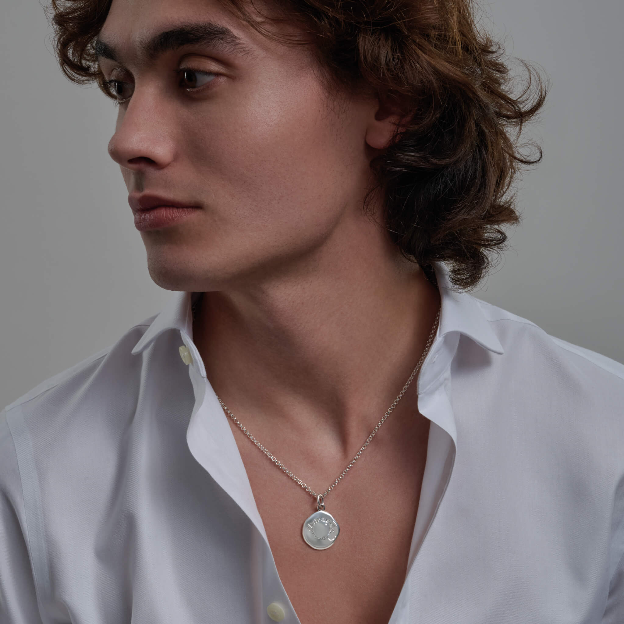 Model wearing a handcrafted round silver pendant necklace engraved with a quote of courage.