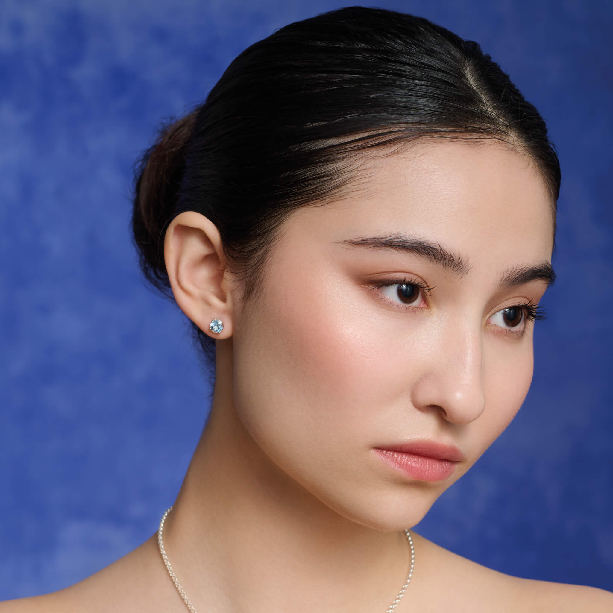 Model wearing handcrafted stud earrings in precious metal with round precious stones.