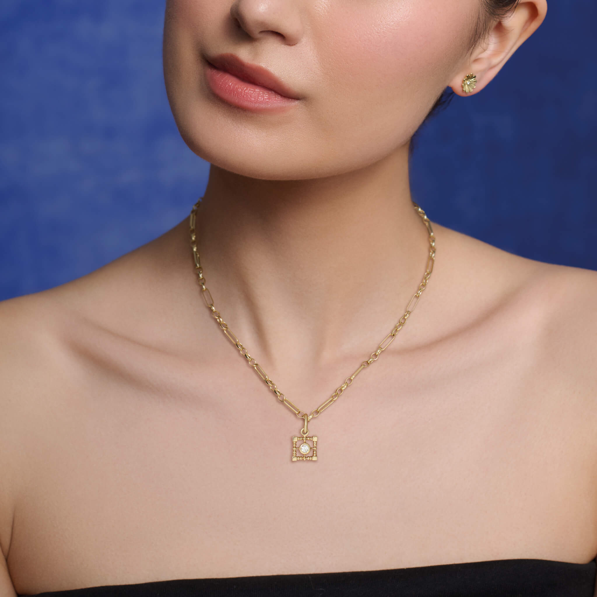 Model wearing a handcrafted necklace pendant featuring a square-shaped frame in yellow gold with a central precious stone.