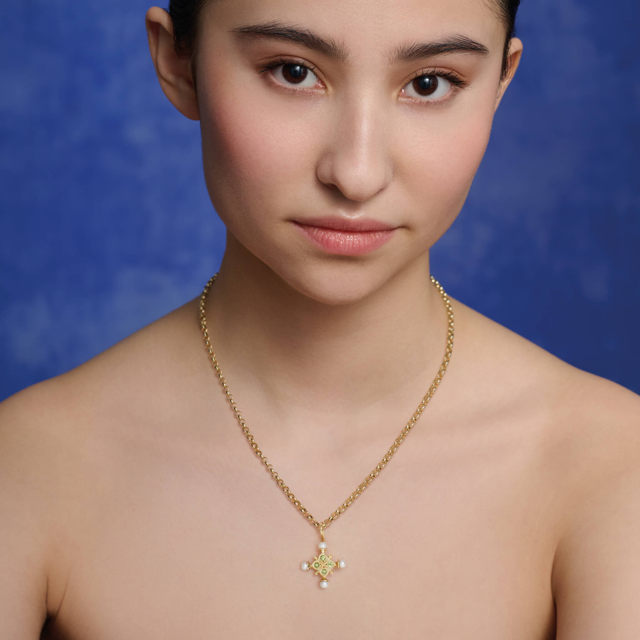 Model wearing a handcrafted cross necklace pendant in yellow gold with a symmetrical arrangement of pearls and precious stones, birthstone of june