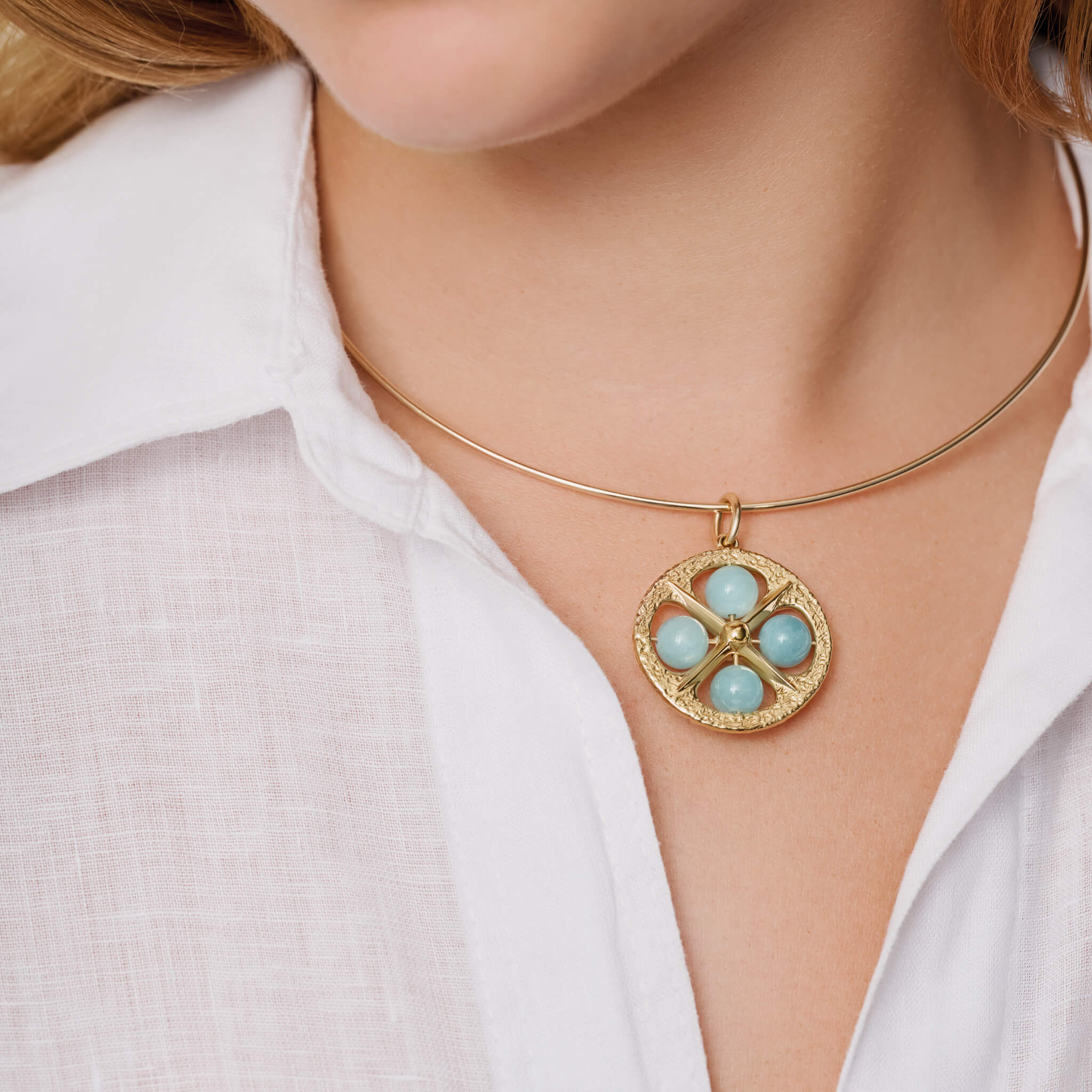 Model wearing handcrafted 9ct yellow gold necklace pendant with a circular motif and a cross in the middle and four aquamarine beads.
