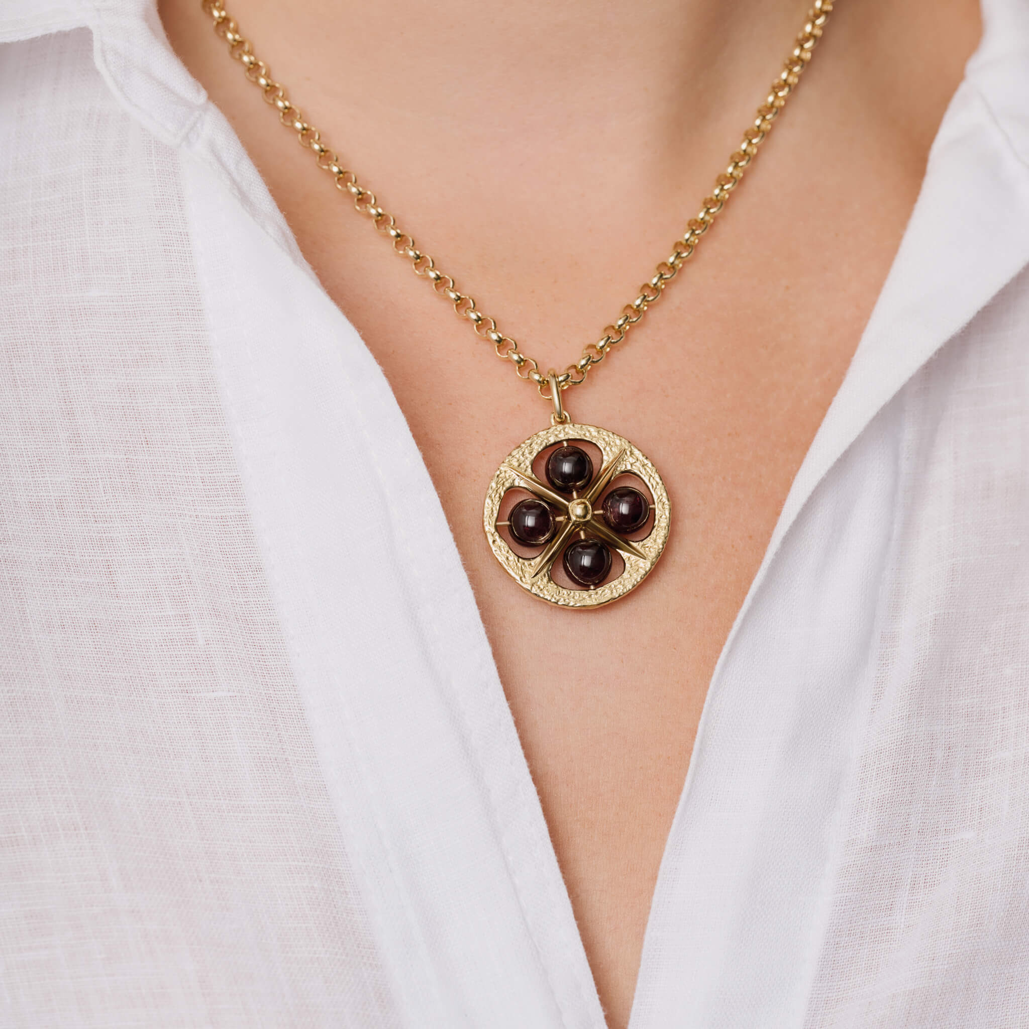 Model wears handcrafted 9ct yellow gold necklace pendant with a circular motif and a cross in the middle and four garnet beads.