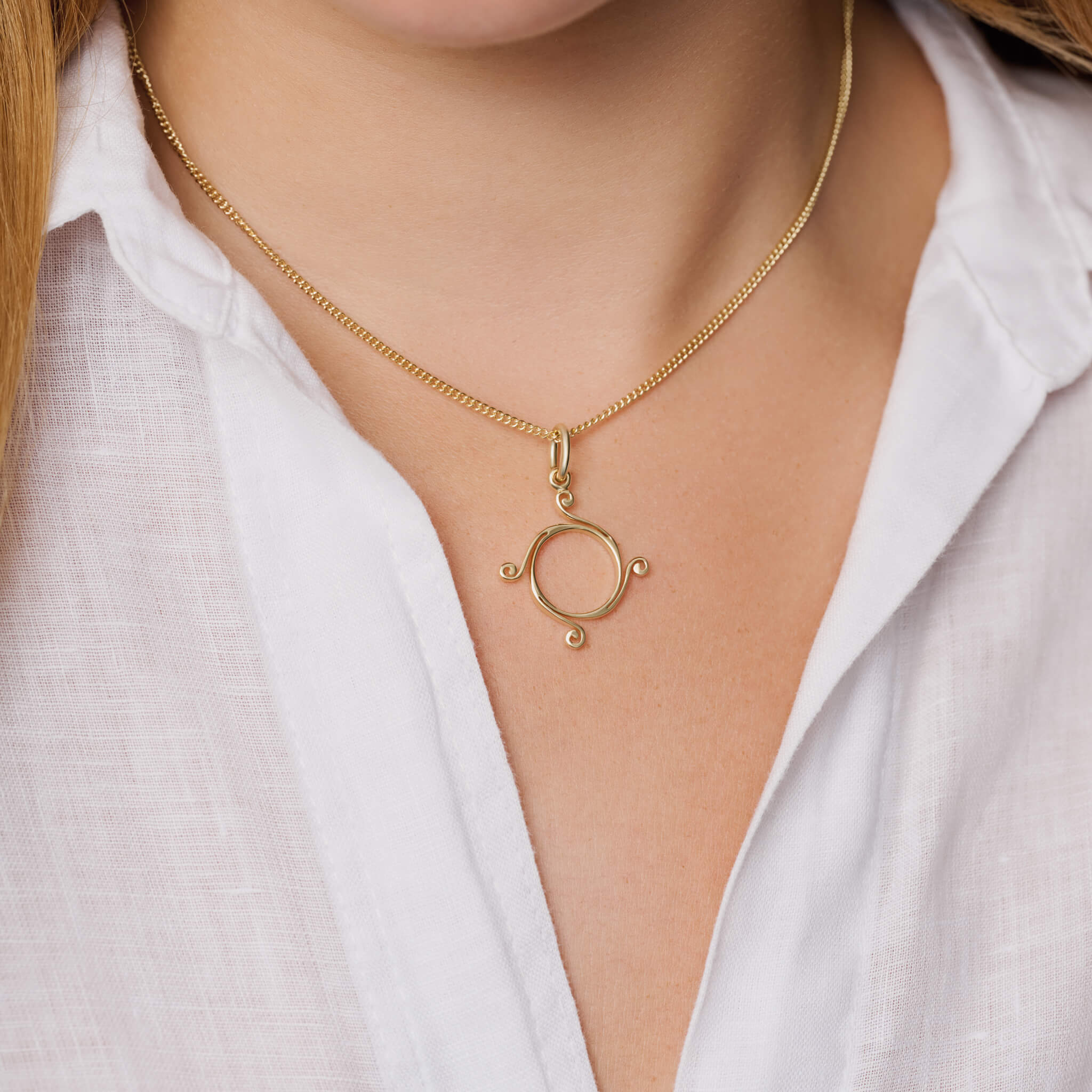 Model wears handcrafted 9ct yellow gold small Athena necklace pendant with a circular shape and spiral at four points.