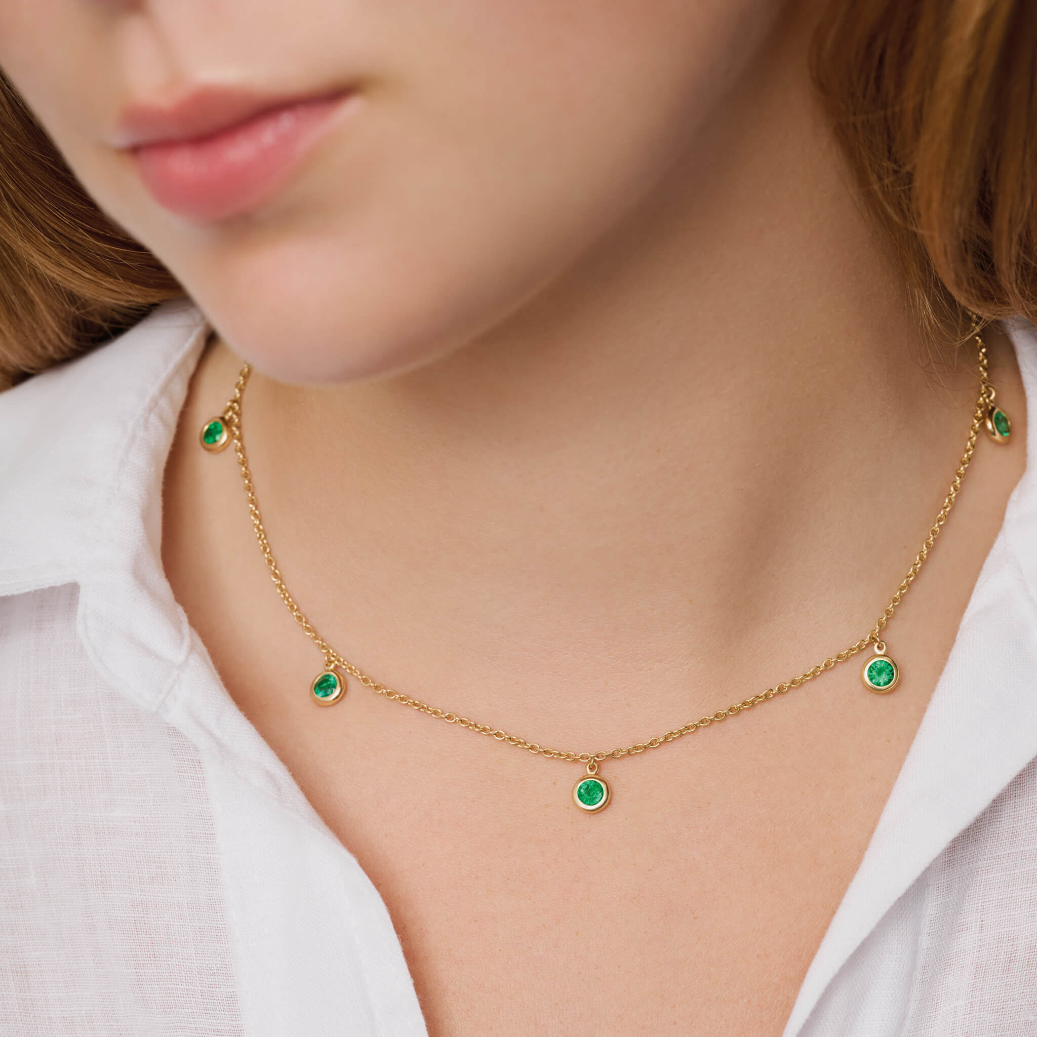Model wears handcrafted 18ct yellow gold necklace with five round emerald drops, birthstone of May.
