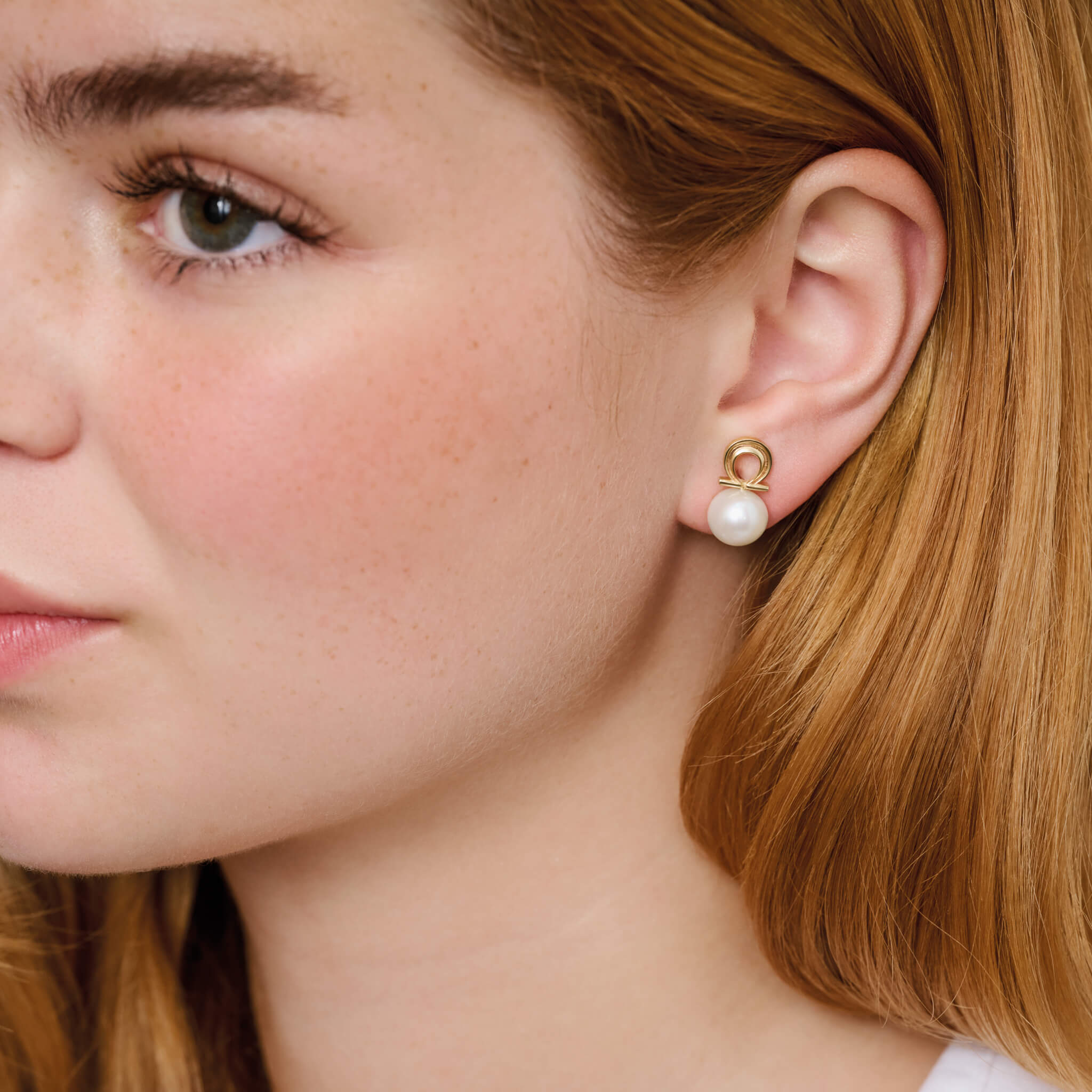 Model wearing handcrafted omega Greek letter shaped stud in silver with white pearl bead.
