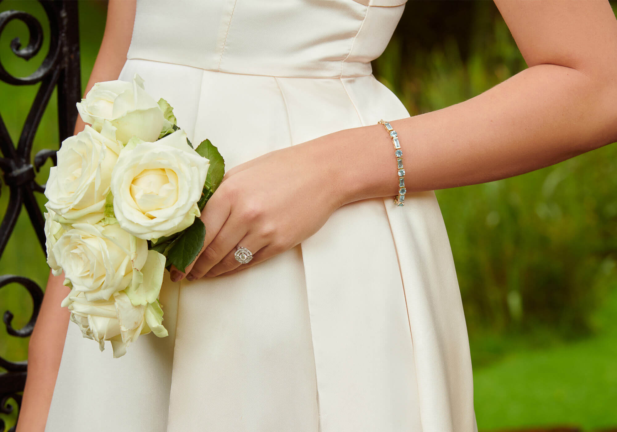 Bride wearing a bracelet adorned with blue precious stones and a diamond ring, holding a bouquet of white flowers.