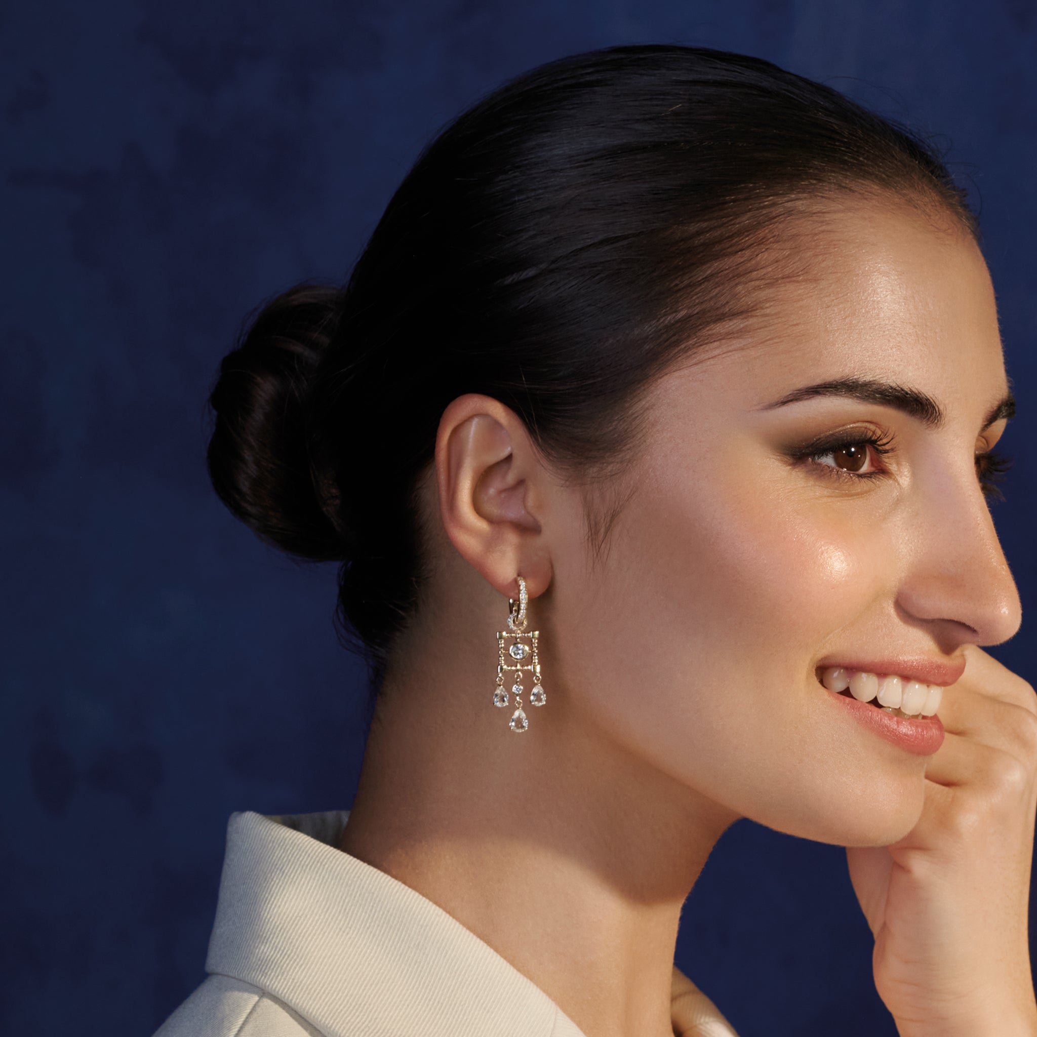 Model wearing handcrafted earring drops in precious metal featuring a teardrop-shaped design with precious stones.