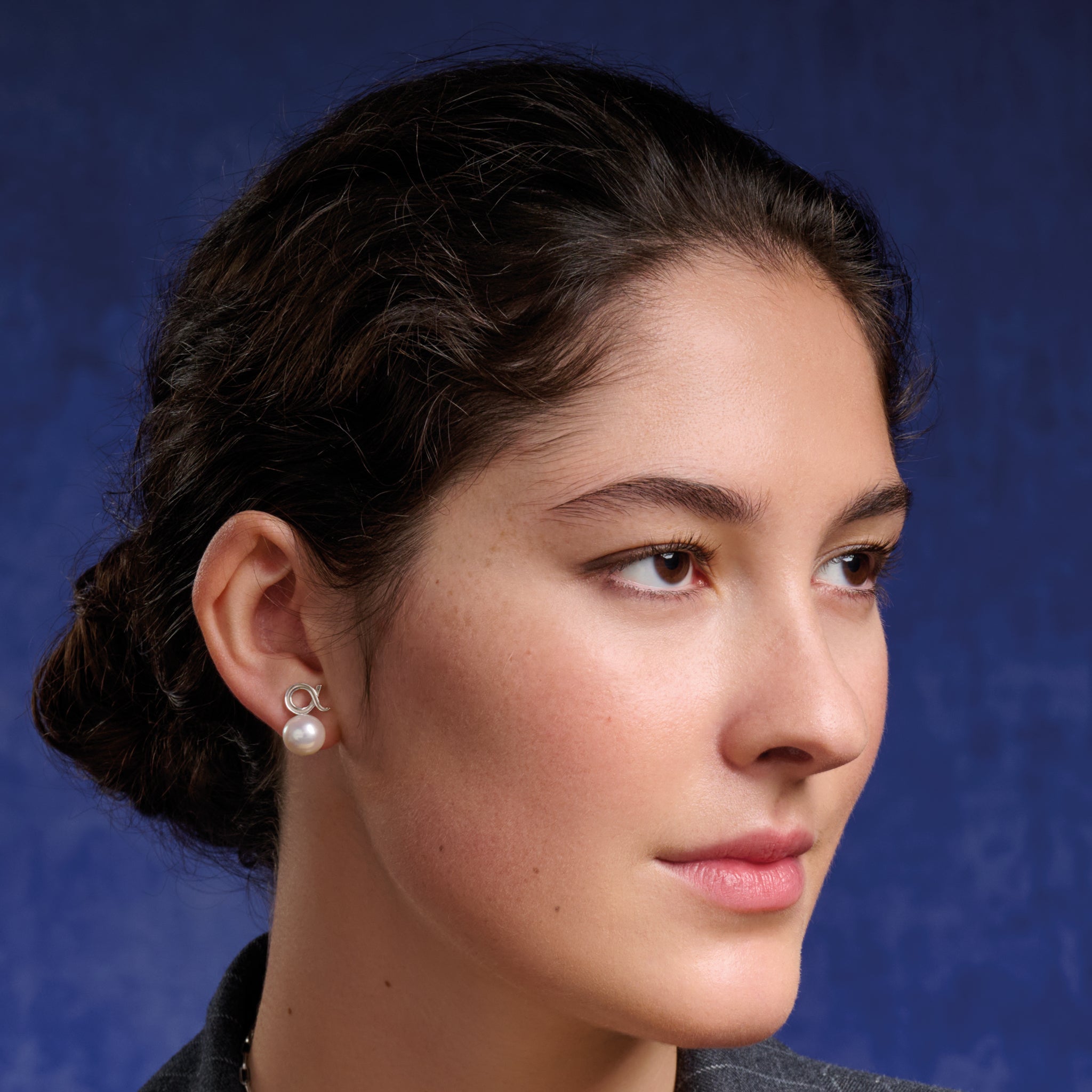 Model wearing handcrafted silver alpha Greek letter shaped stud with white pearl bead.