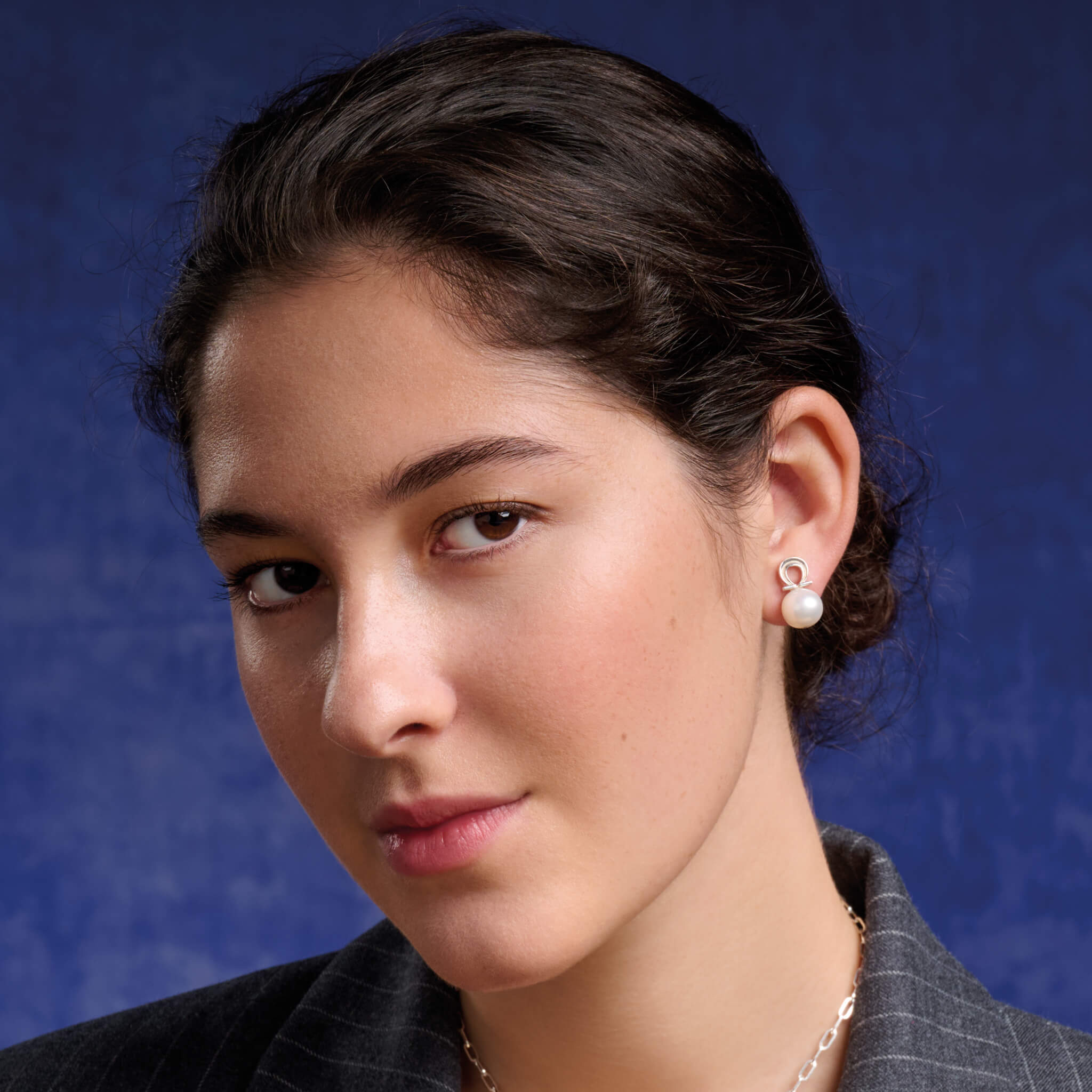 Model wearing handcrafted silver alpha Greek letter shaped stud with white pearl bead.