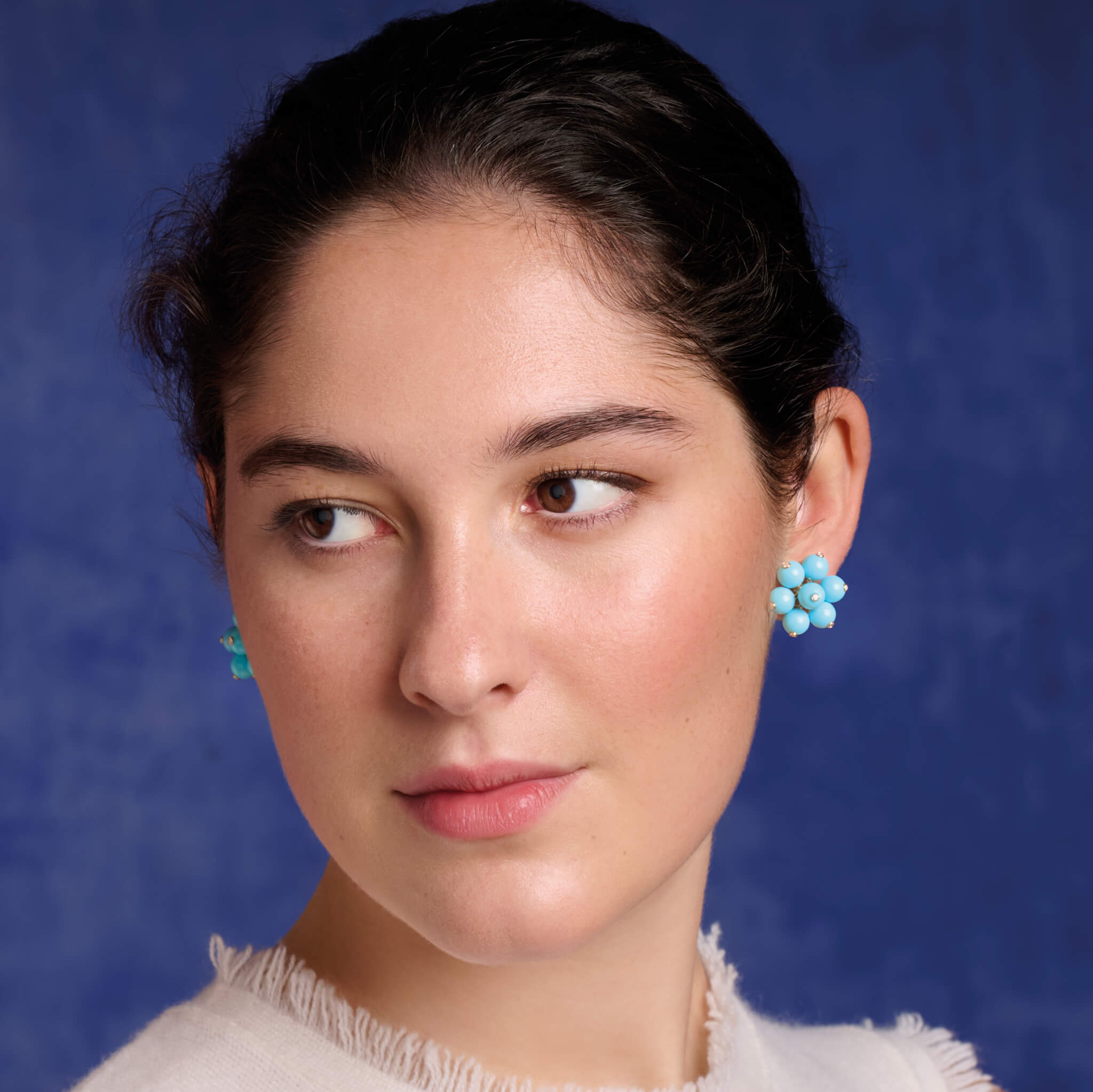 Model wearing handcrafted earrings in 18ct yellow gold featuring a cluster of turqouise beads, the birthstone of December. The beads are interspersed with small diamonds.