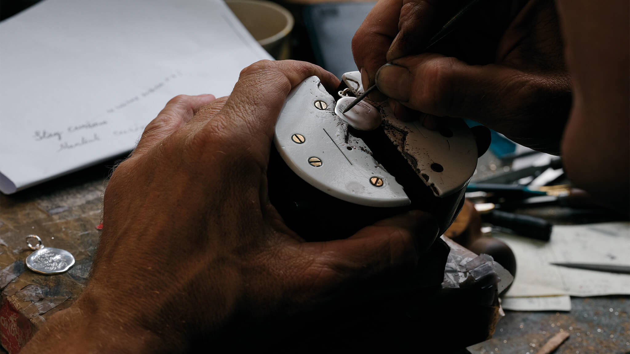 Craftsman hand engraving a silver necklace pendant in a London workshop.