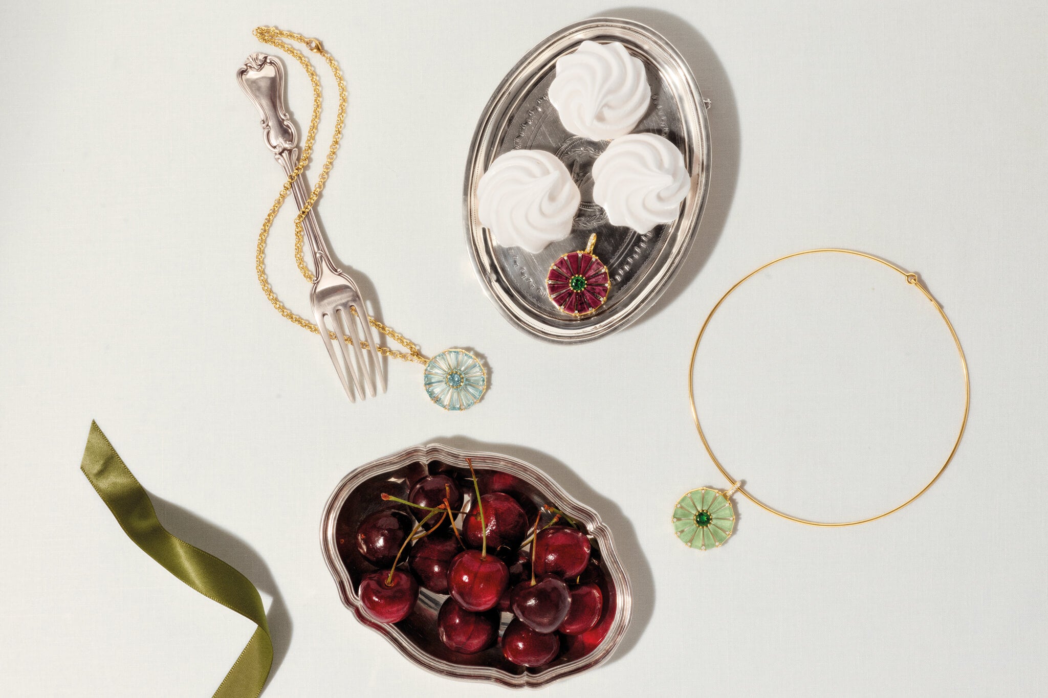 Roi Soleil pendants in yellow gold with different colourful gemstones on a background with silver trays and cutlery