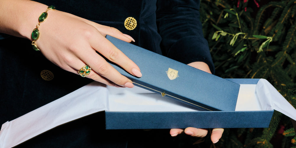 Cassandra Goad gift box being unwrapped near Christmas tree, model wearing Marina Bracelet 18ct Yellow Gold Oval Cabochon Strong Green Tourmaline and Multi Aeneus Ring 18ct Yellow Gold Green Sapphire & Diamond