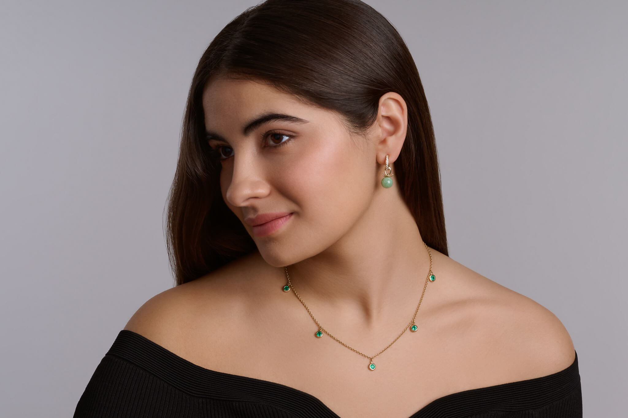 Model wearing a handcrafted 18ct yellow gold necklace featuring five fine green emerald drops and earring drops with emerald beads.