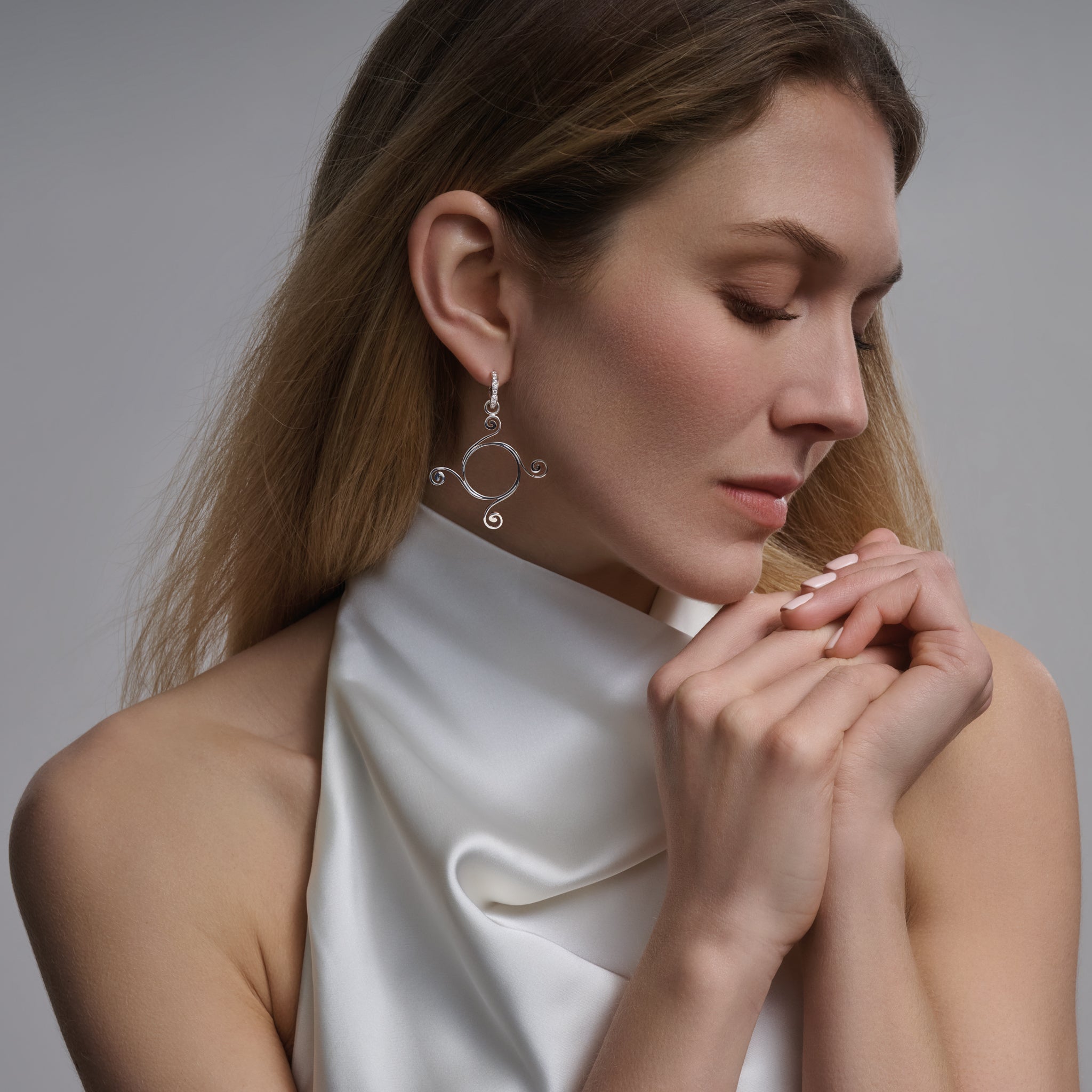 Model wearing handcrafted 9ct yellow gold earring drops with a circular shape and spiral at four points, hanging from hoop earrings.