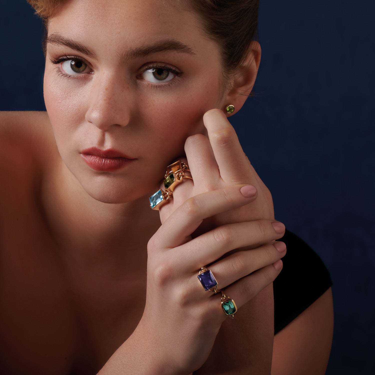 Model wearing handcrafted rings in precious metals featuring central precious stones.