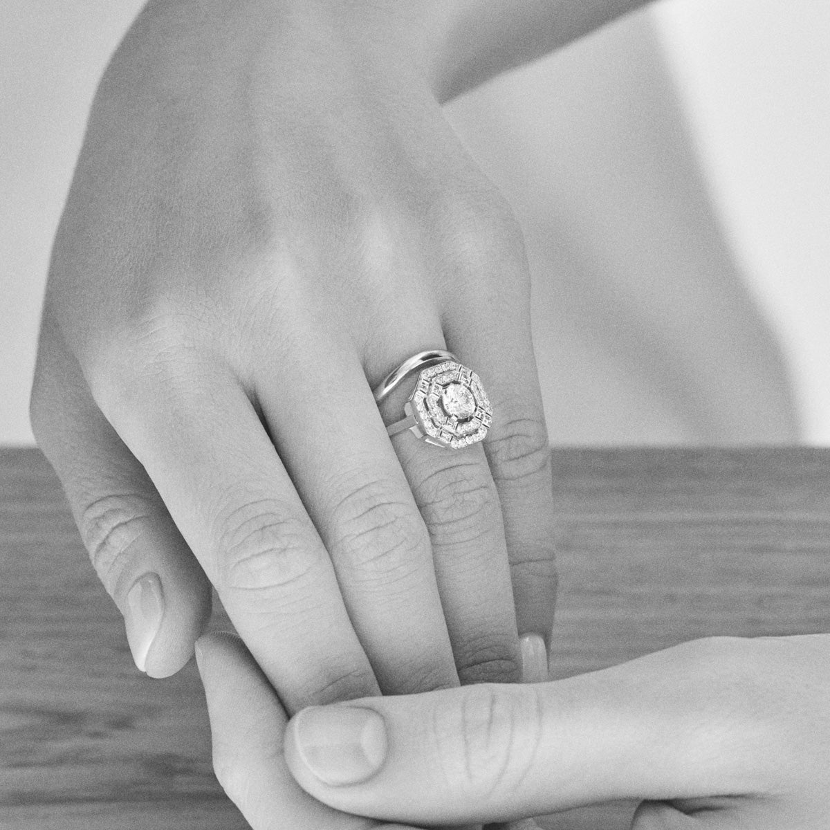 A man and woman’s hands displaying an engagement ring on her finger, with focus on the ring.