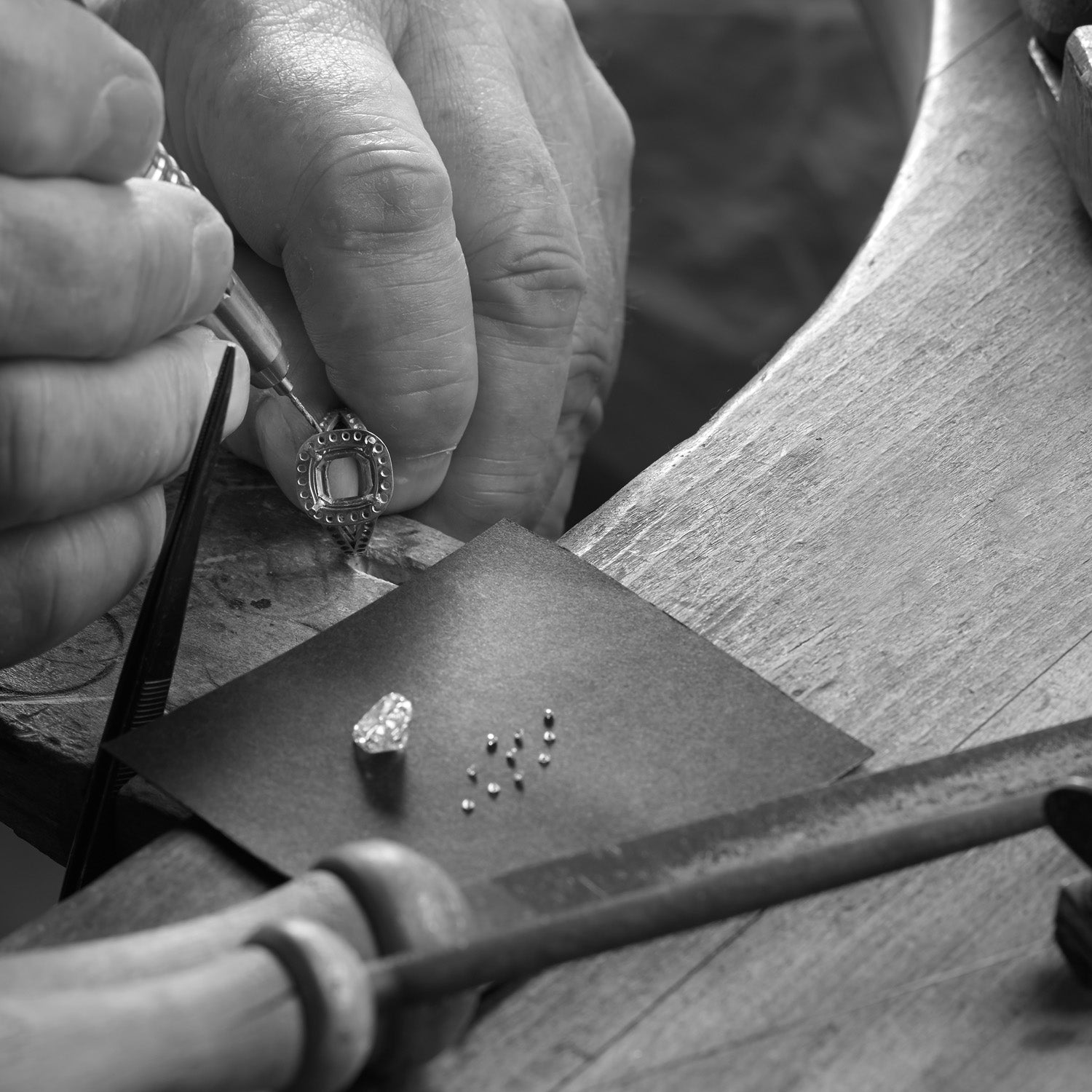 A craftsman setting precious stones into an engagement ring, with loose diamonds placed beside the ring on the workbench in London.