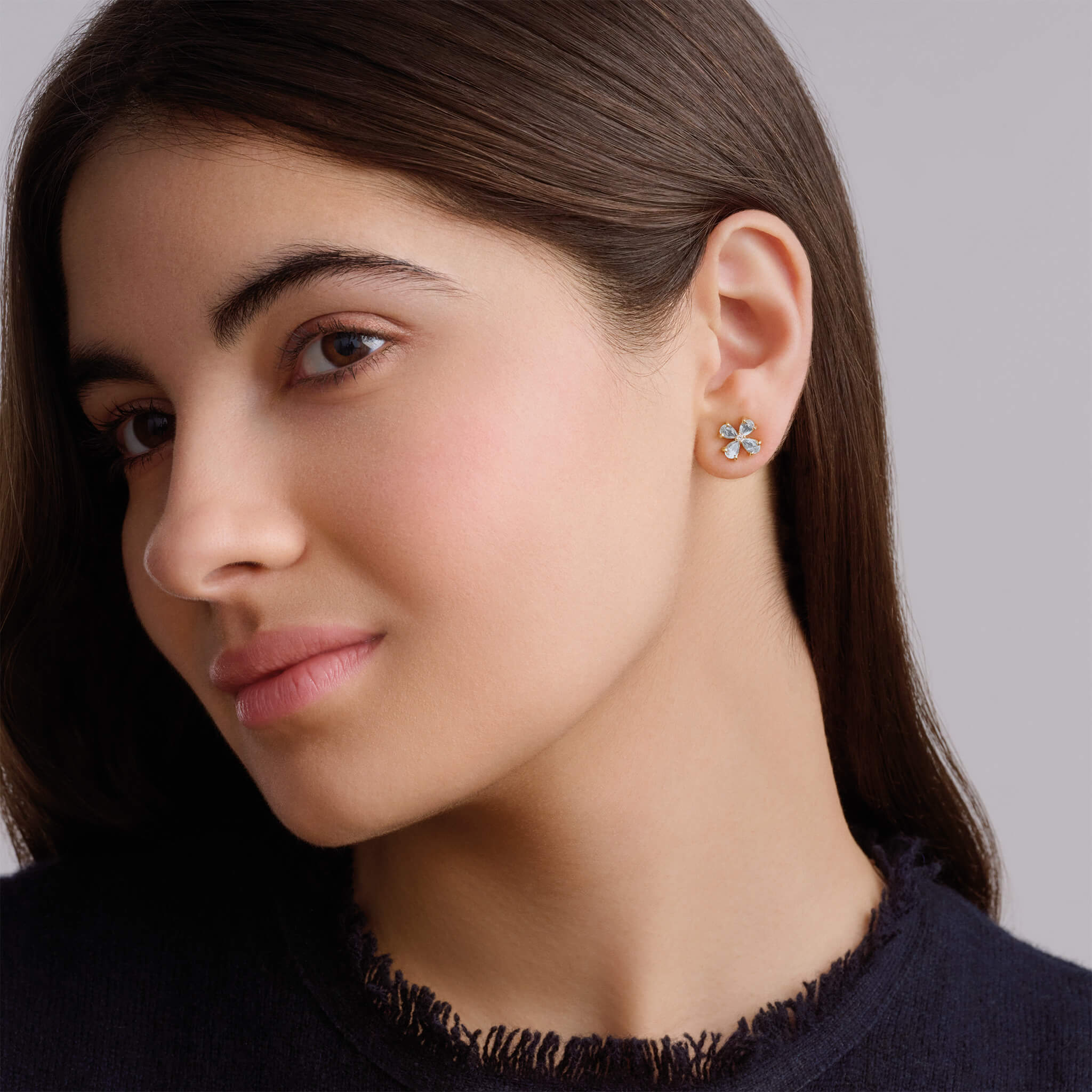 Model wearing handcrafted four-leaf clover earring studs in precious metal with precious stones.