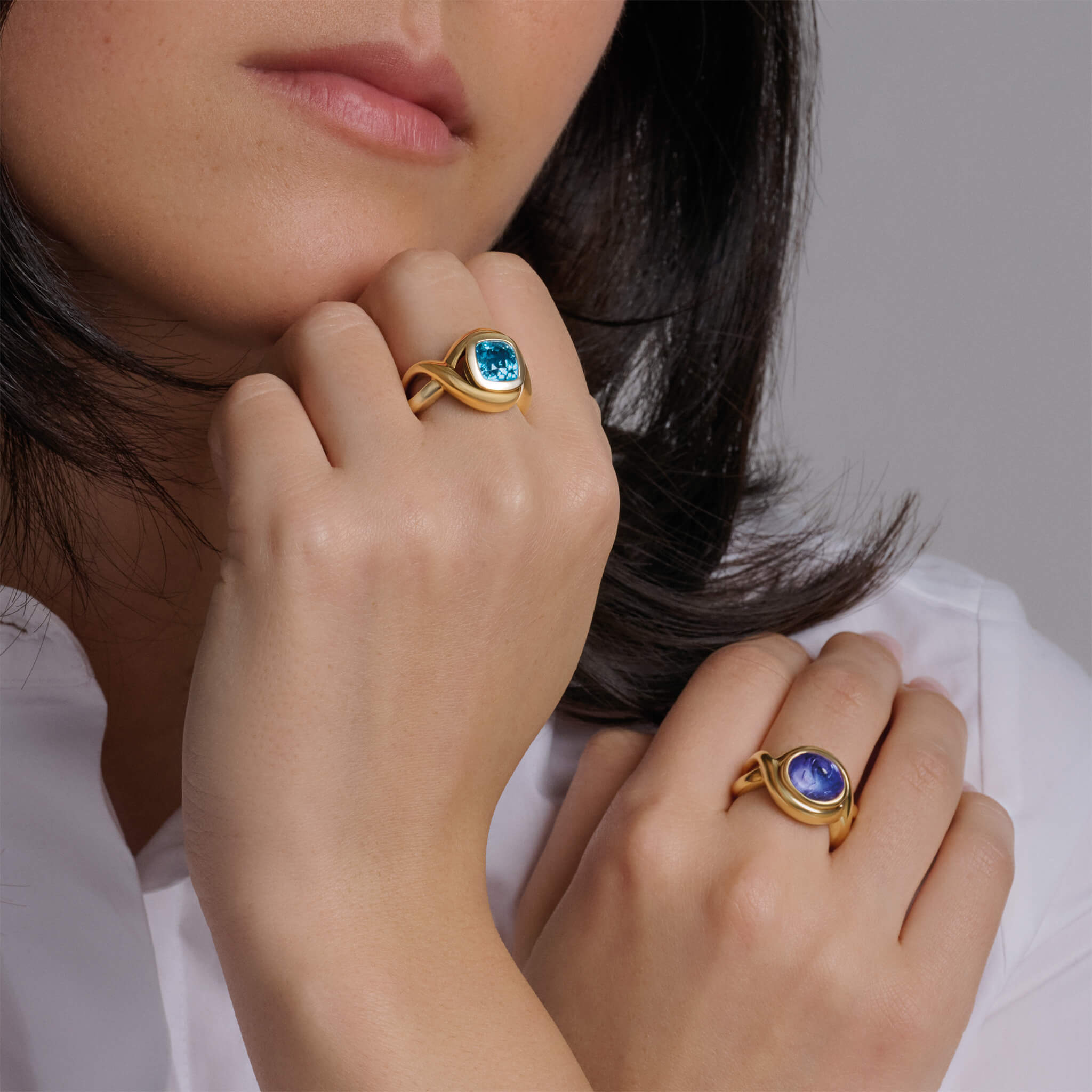 Model wearing handcrafted rings in precious metal featuring curved shanks with round precious stones.