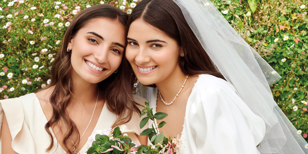 A bride and her bridesmaid sitting together, both elegantly adorned in pearl and diamond jewellery.