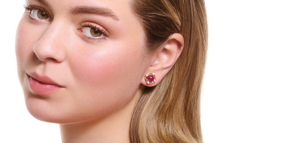 model wearing cabochon ruby studs with yellow gold halo