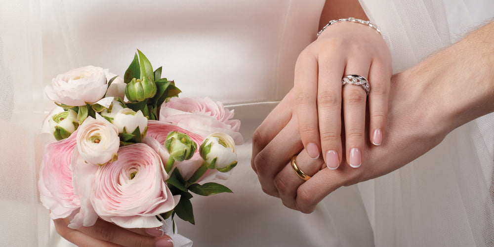 Hand laying on top of man hand while holding a bouquet of flowers and showcasing wedding bands