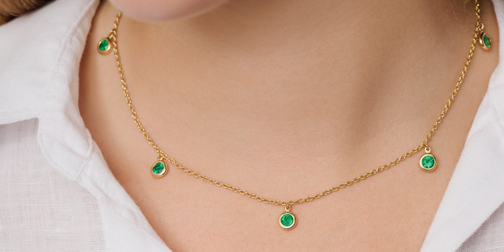 Model wearing a handcrafted yellow gold necklace featuring a facetted emeralds birthstone of May.