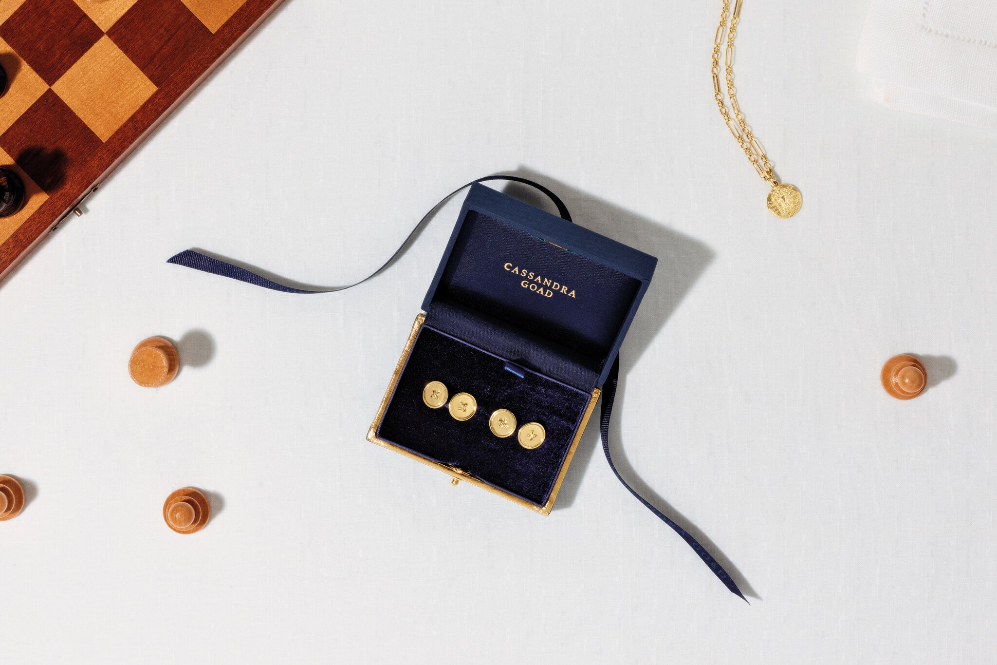 Yellow gold cufflinks in Cassandra Goad gift box, with yellow gold medallion charm necklace and chess pieces in the background