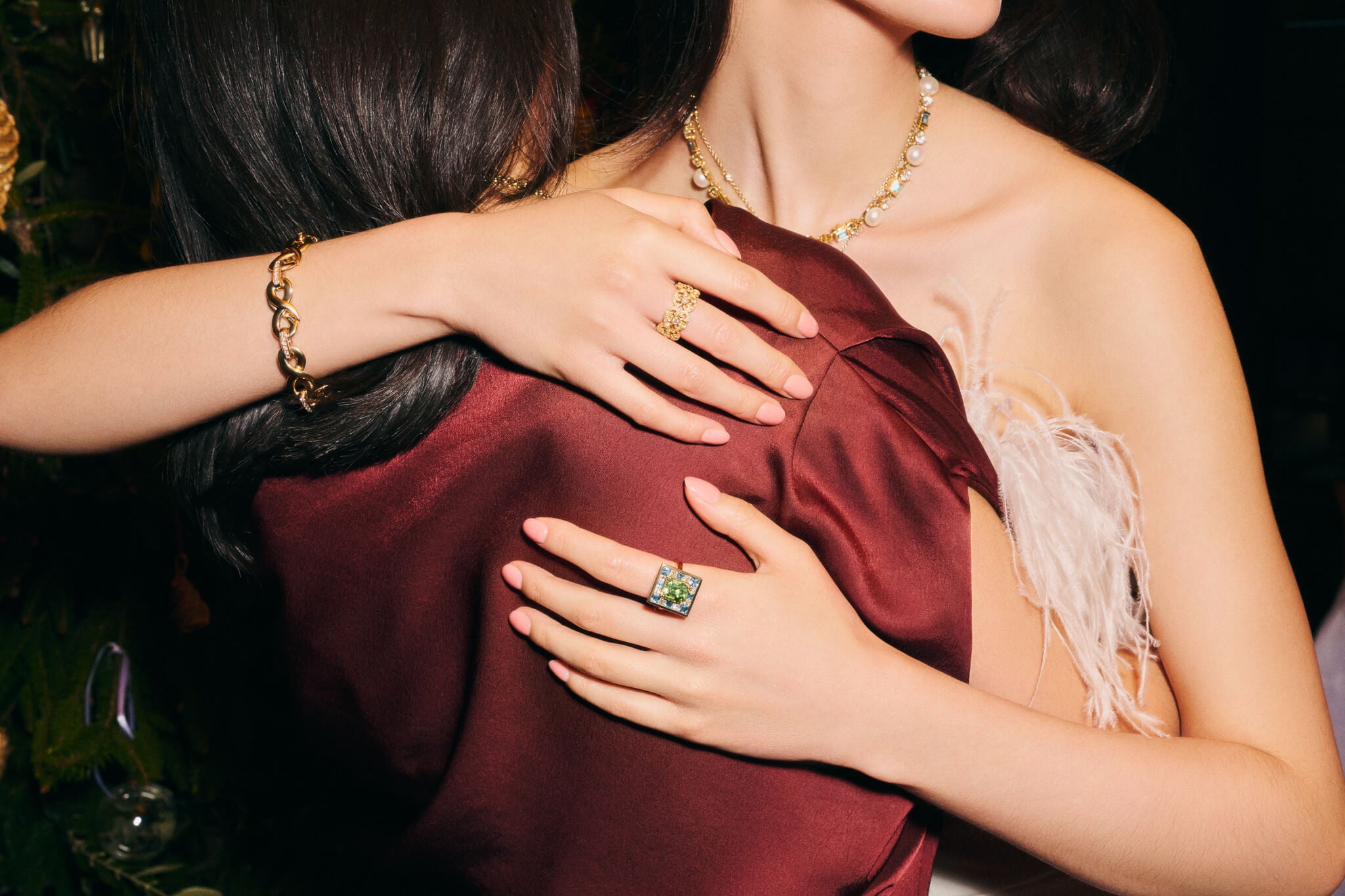 Two models embrace at a Christmas party wearing Cassandra Goad High Jewellery including the Place des Vosges cocktail ring and Serpent Geneve bracelet with diamond and ruby.