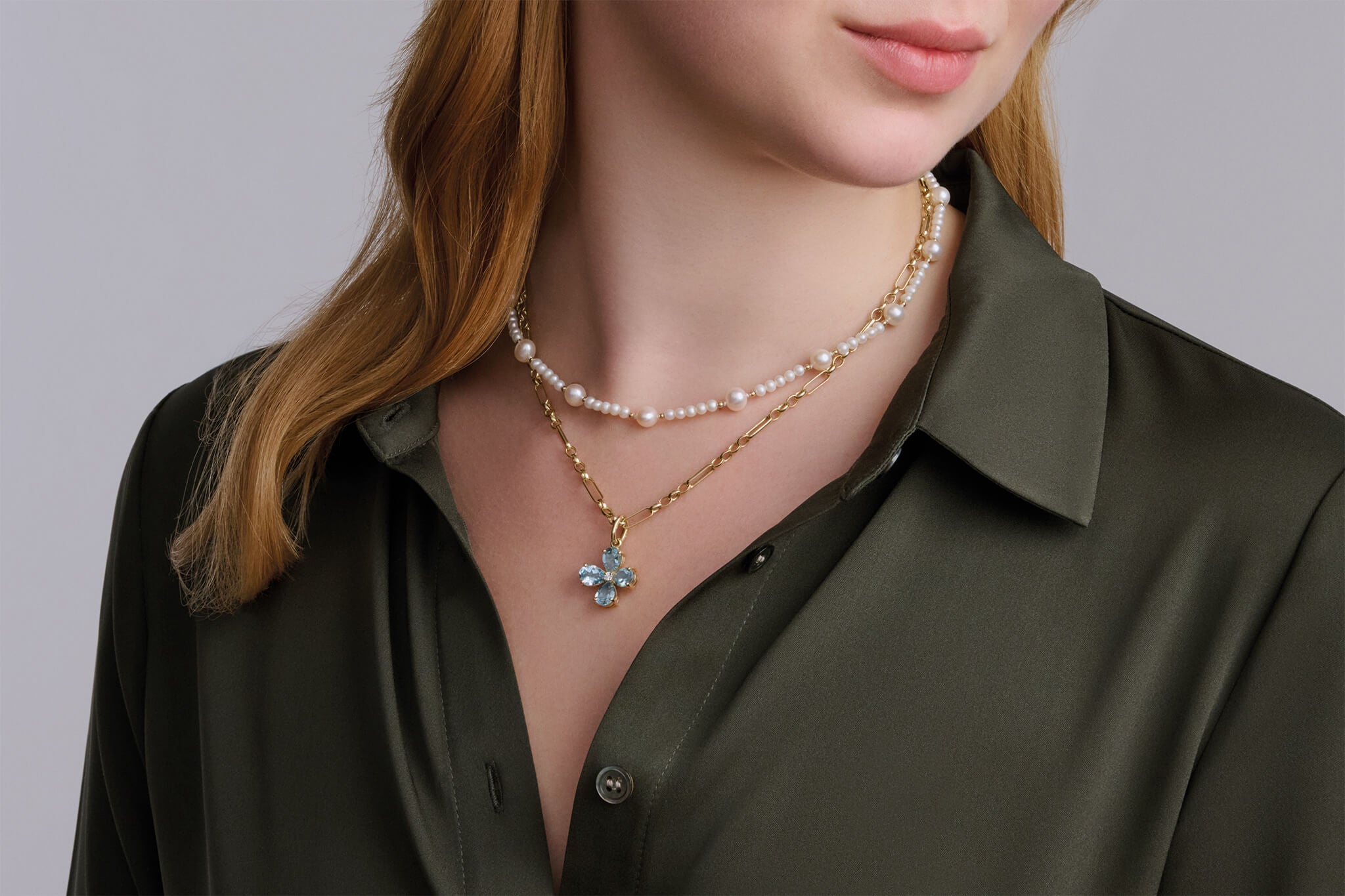 Model wearing layered necklaces and chain and pendants with blue topaz and pearl gemstones.